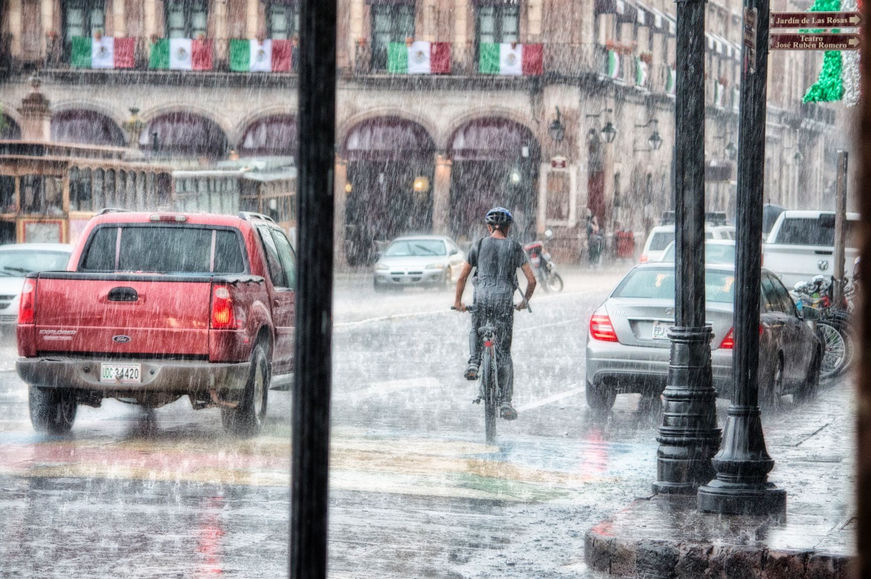 Person riding their bicycle in the rain as cars drive by.
Credit- Pexels