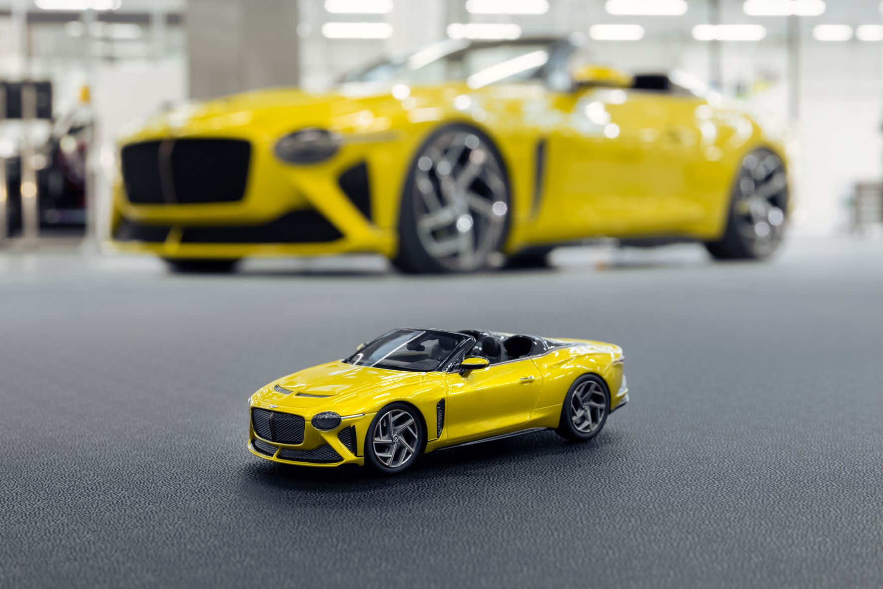 A close-up of a Yellow Flame Bentley Mulliner Bacalar pictured with a full-size car in the background.