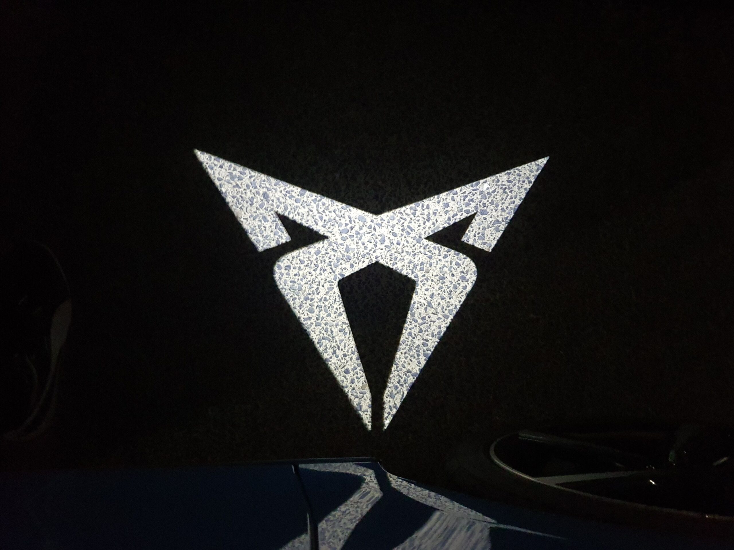 Illuminated Cupra logo puddle lighting on the ground.