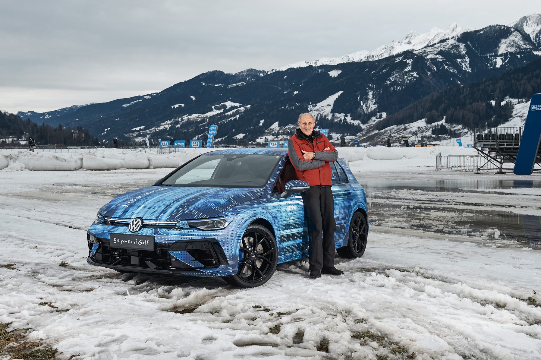 German motorsport legend Hans-Joachim Stuck standing next to a Mk 8 Volkswagen Golf R in camouflage.