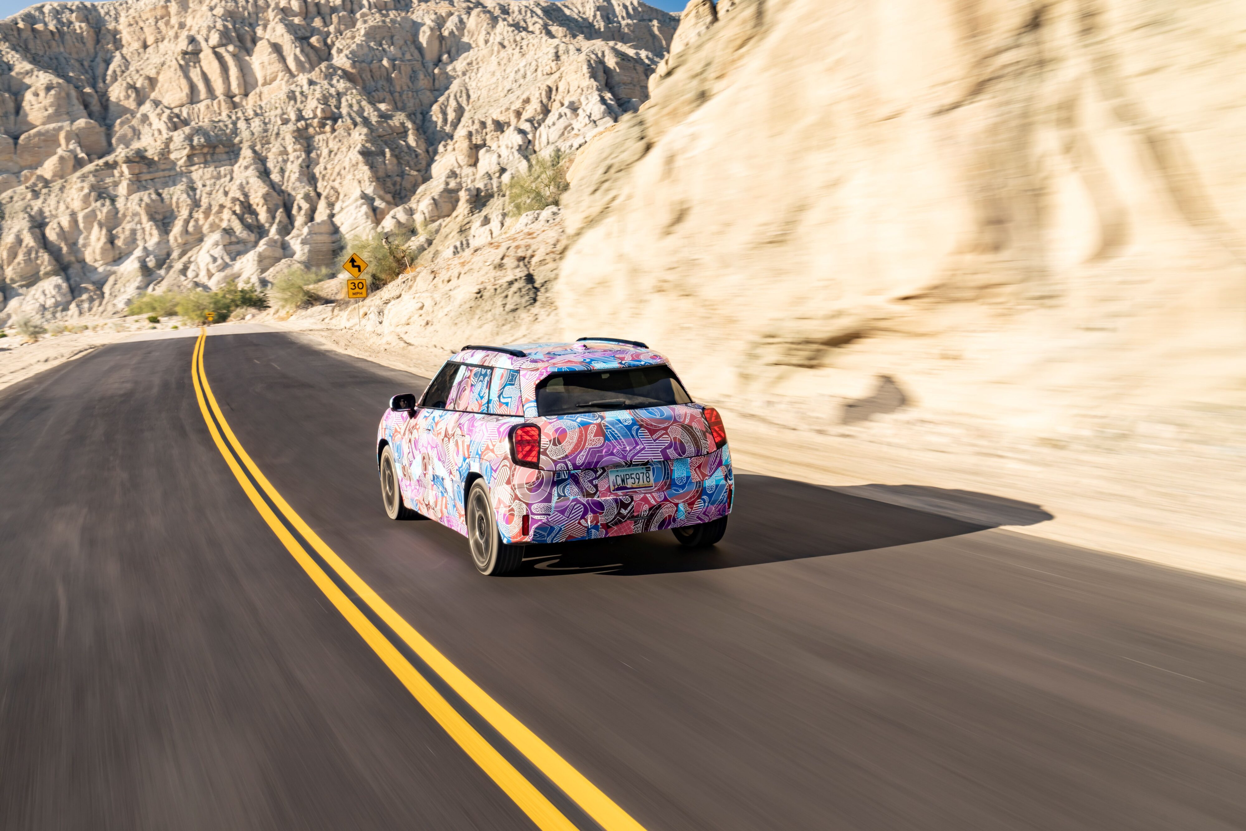 Rear three quarters photo of a camouflaged prototype MINI Aceman EV in a desert setting.