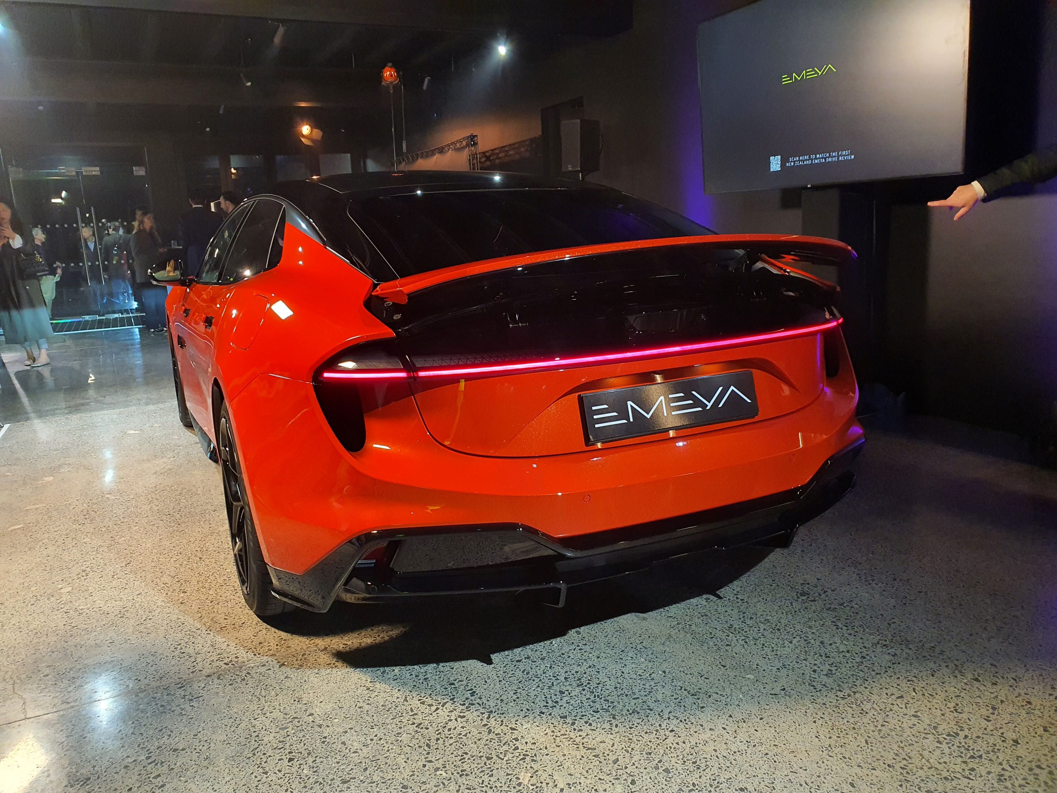Rear three quarters view of a Lotus Emeya S in Hyperglow Orange at Lotus Auckland.