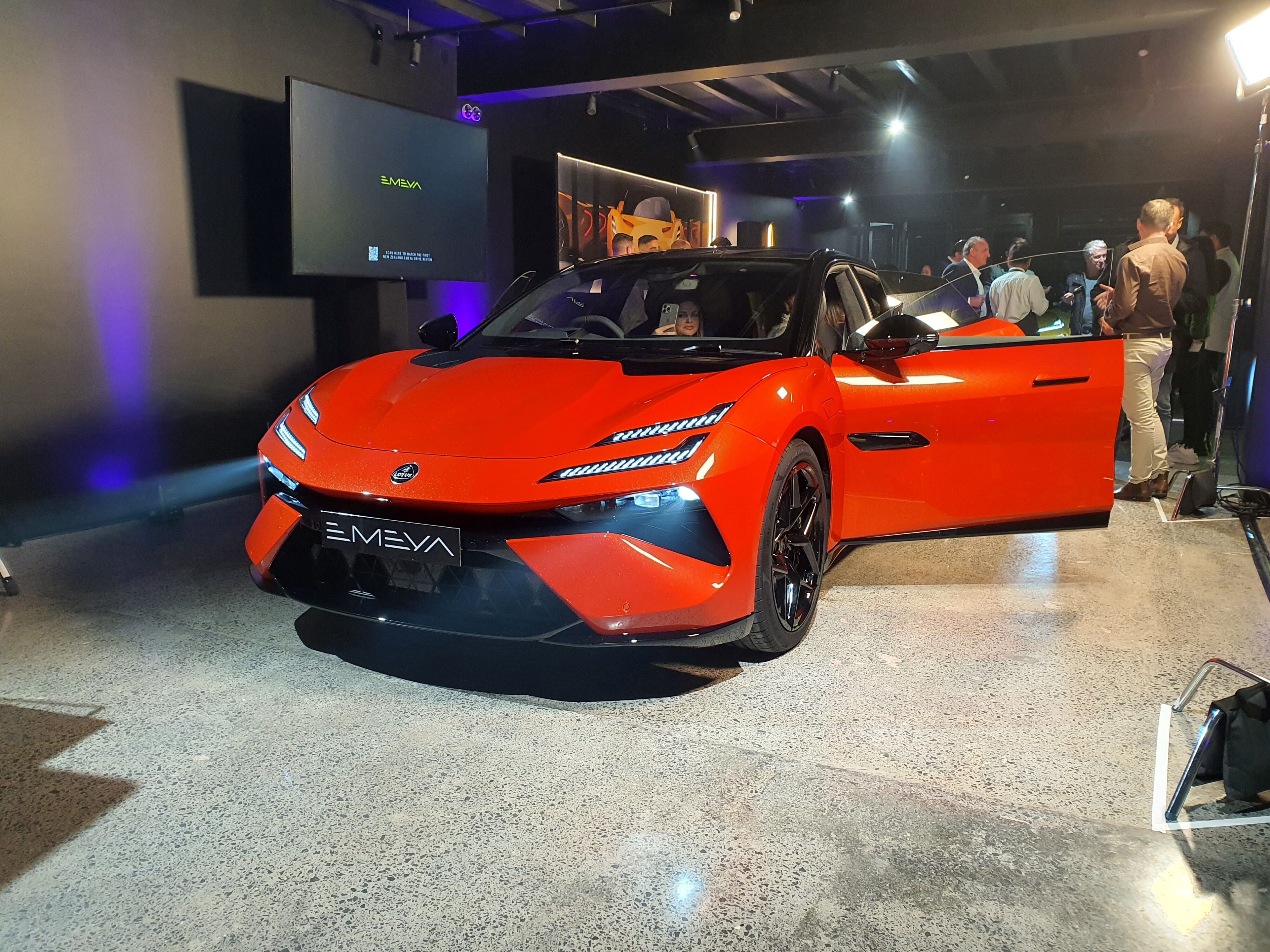 Front three quarters view of a 2024 Lotus Emeya S in Fireglow Orange at Lotus Auckland.