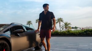 A model dressed in Lamborghini x Orlebar Brown clothing posing by a Lamborghini Huracan Sterrato.