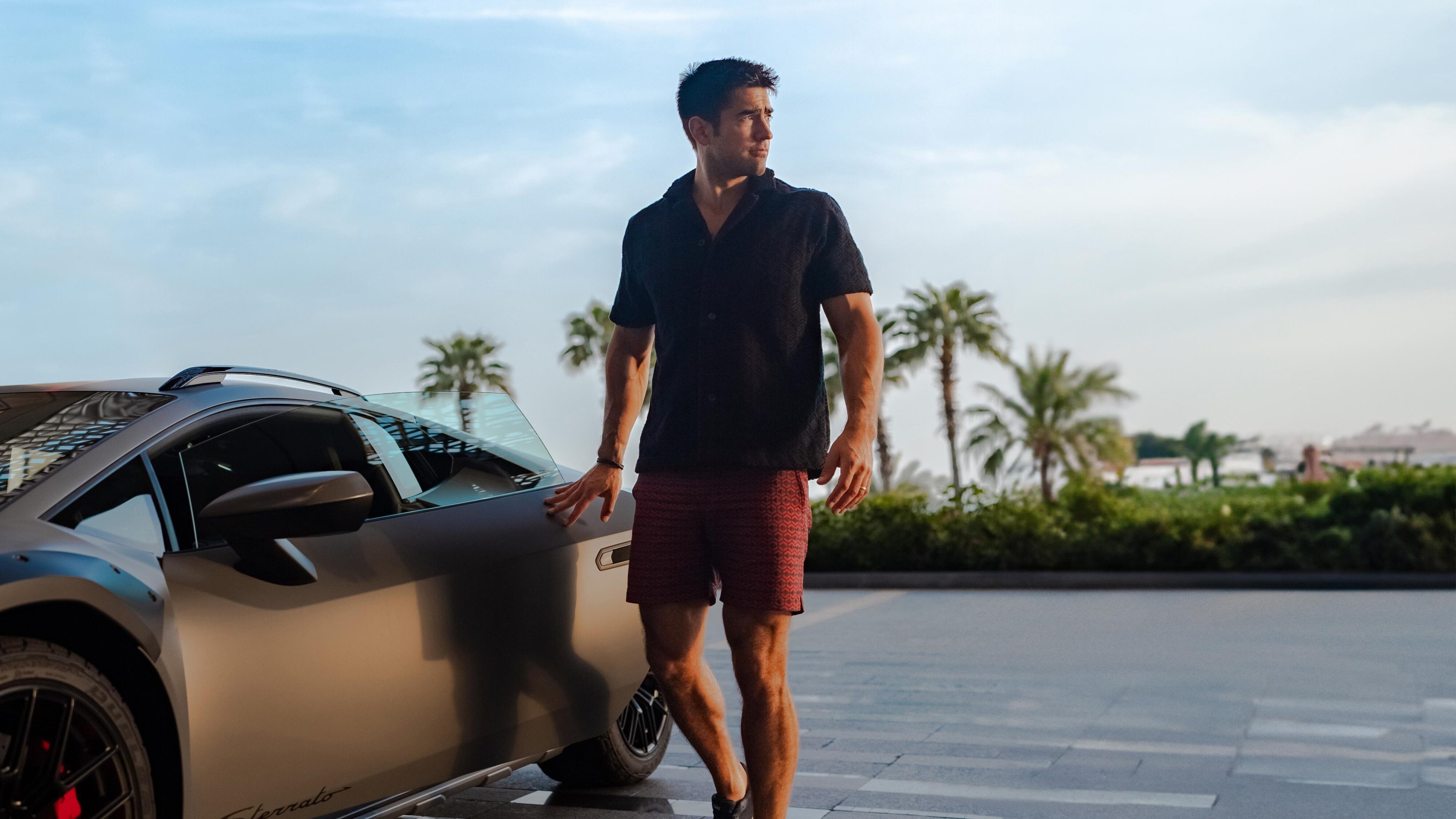 A model dressed in Lamborghini x Orlebar Brown clothing posing by a Lamborghini Huracan Sterrato.