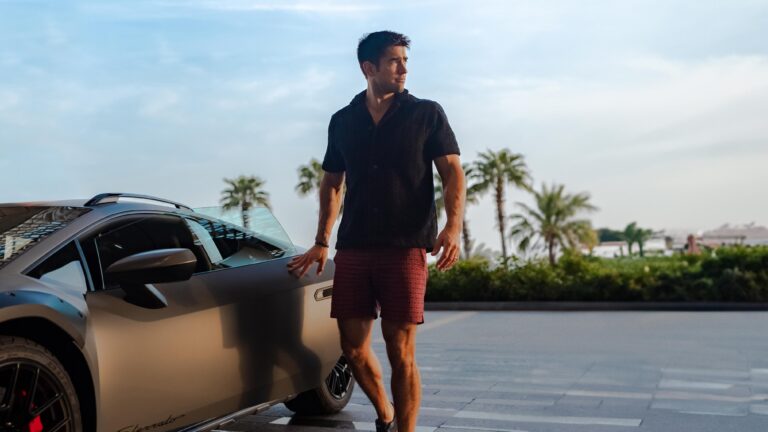 A model dressed in Lamborghini x Orlebar Brown clothing posing by a Lamborghini Huracan Sterrato.