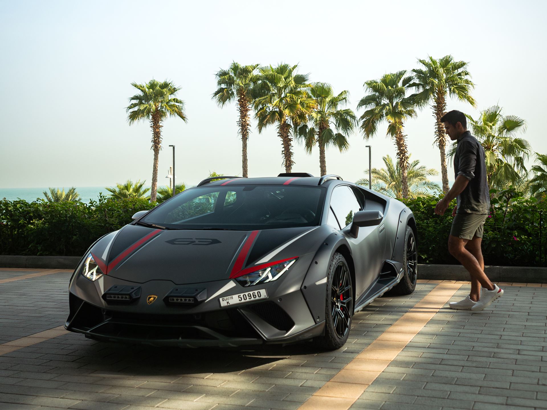 A model dressed in Lamborghini by Orlebar Brown walks up to a Lamborghini Huracan Sterrato.