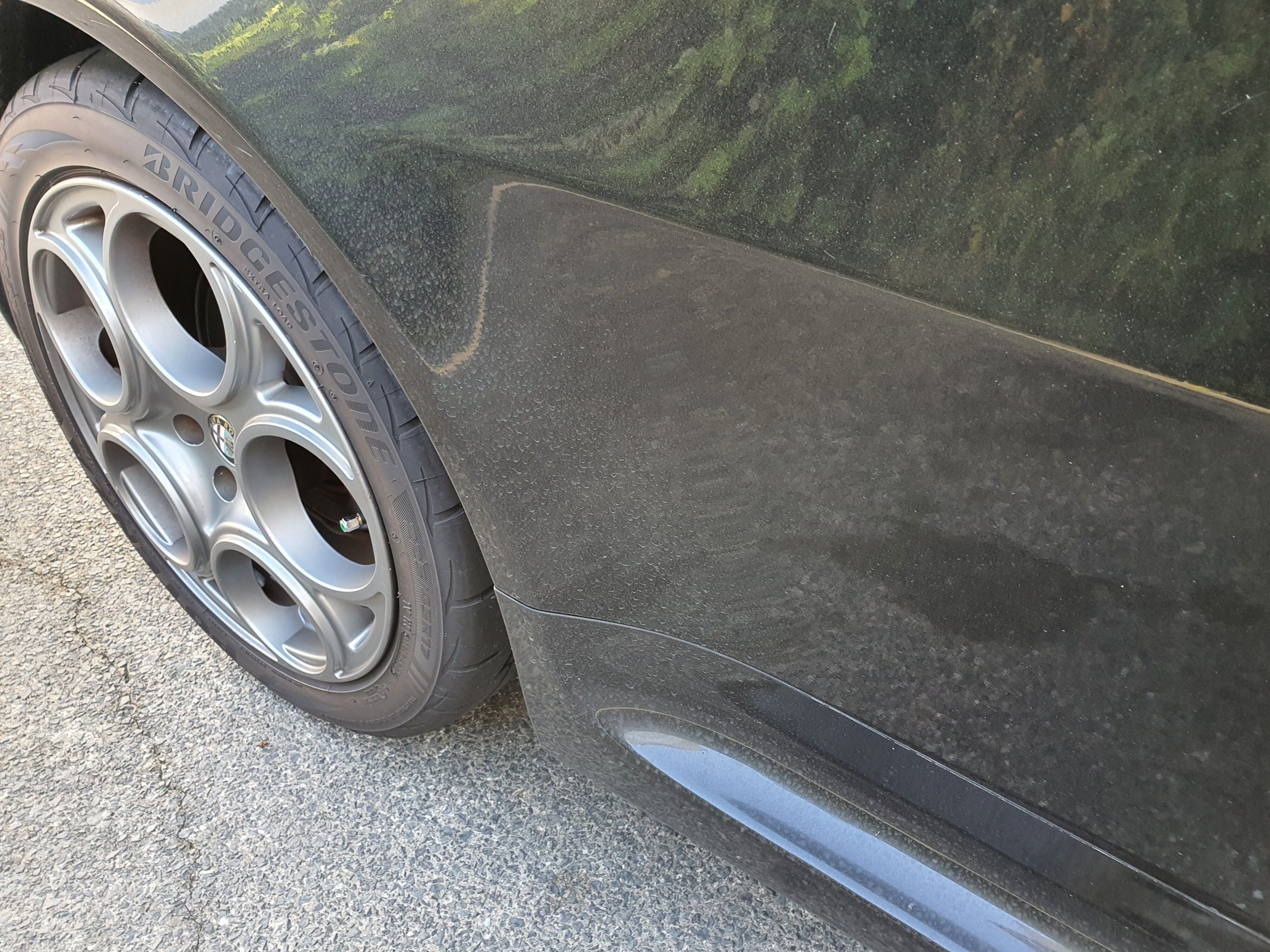 An unclean right rear wheel arch on a black 2004 Alfa Romeo 147 GTA.