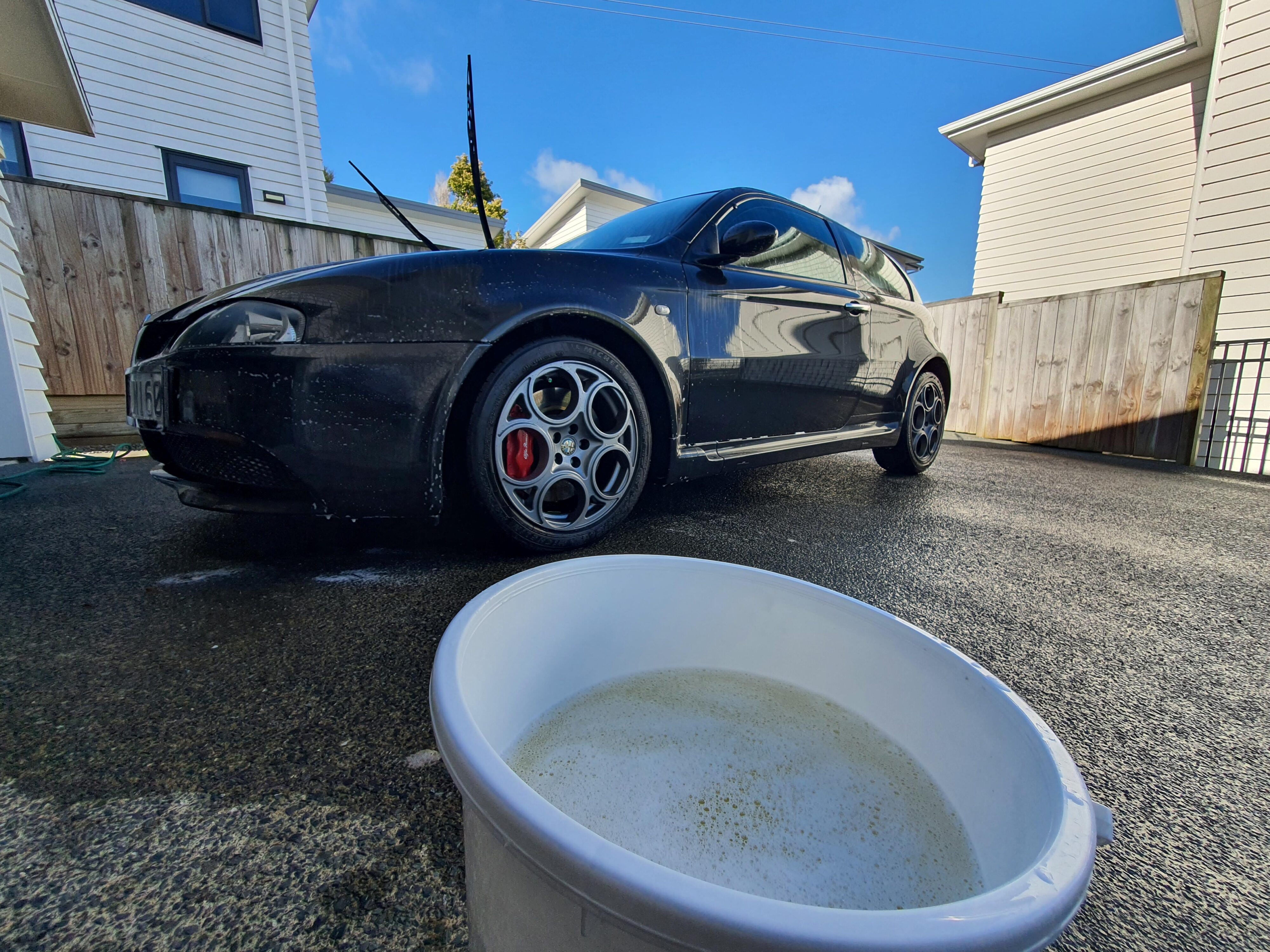 A photo of Armor All's new Wash & Wax solution mixed with water in a bucket with an Alfa Romeo 147 GTA in the background.