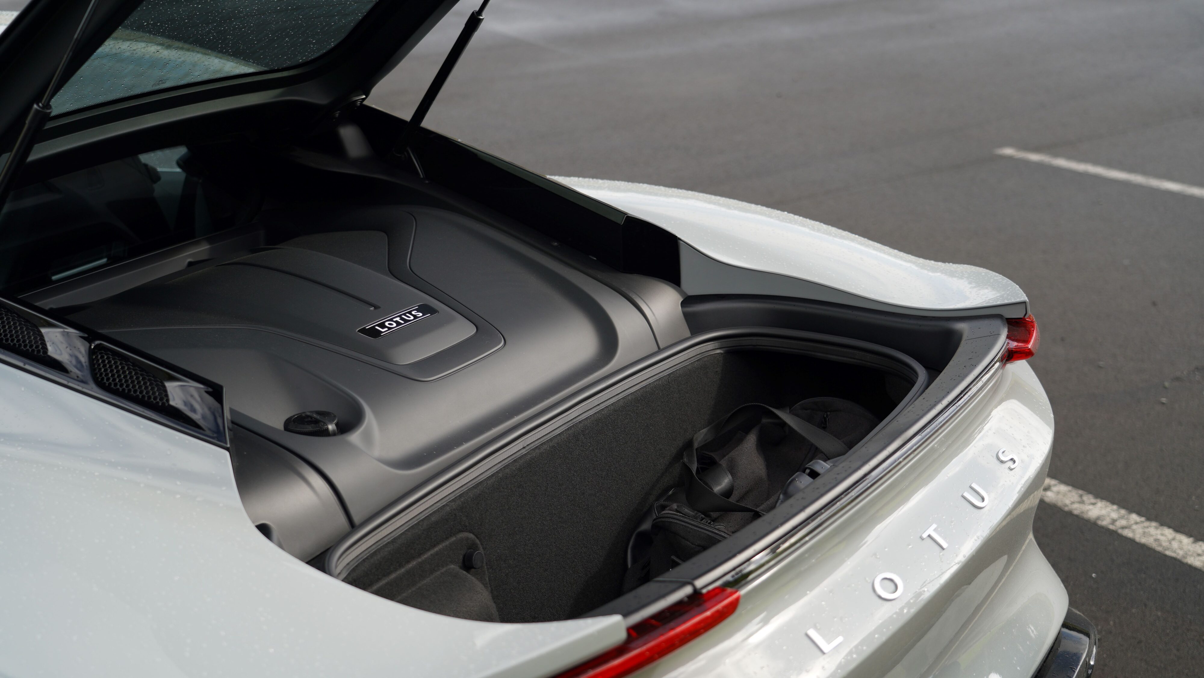 Photo of the rear hatch open on a 2024 Lotus Emira i4 Turbo showing the trunk space and engine cover.