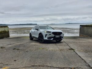Front three quarters view of a 2024 Cupra Formentor V e-Hybrid on a boat ramp with a gloomy ocean background.