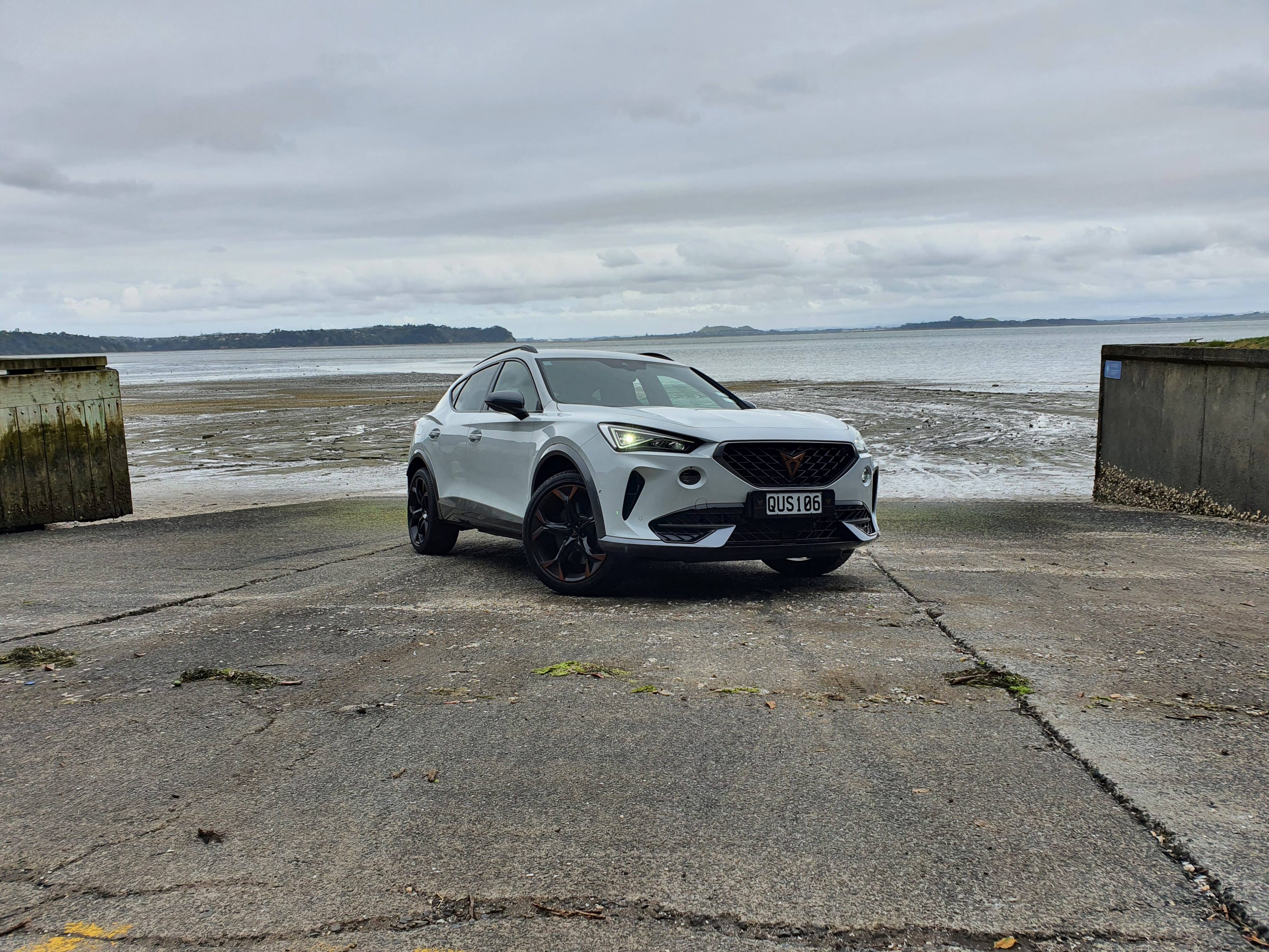 Front three quarters view of a 2024 Cupra Formentor V e-Hybrid on a boat ramp with a gloomy ocean background.