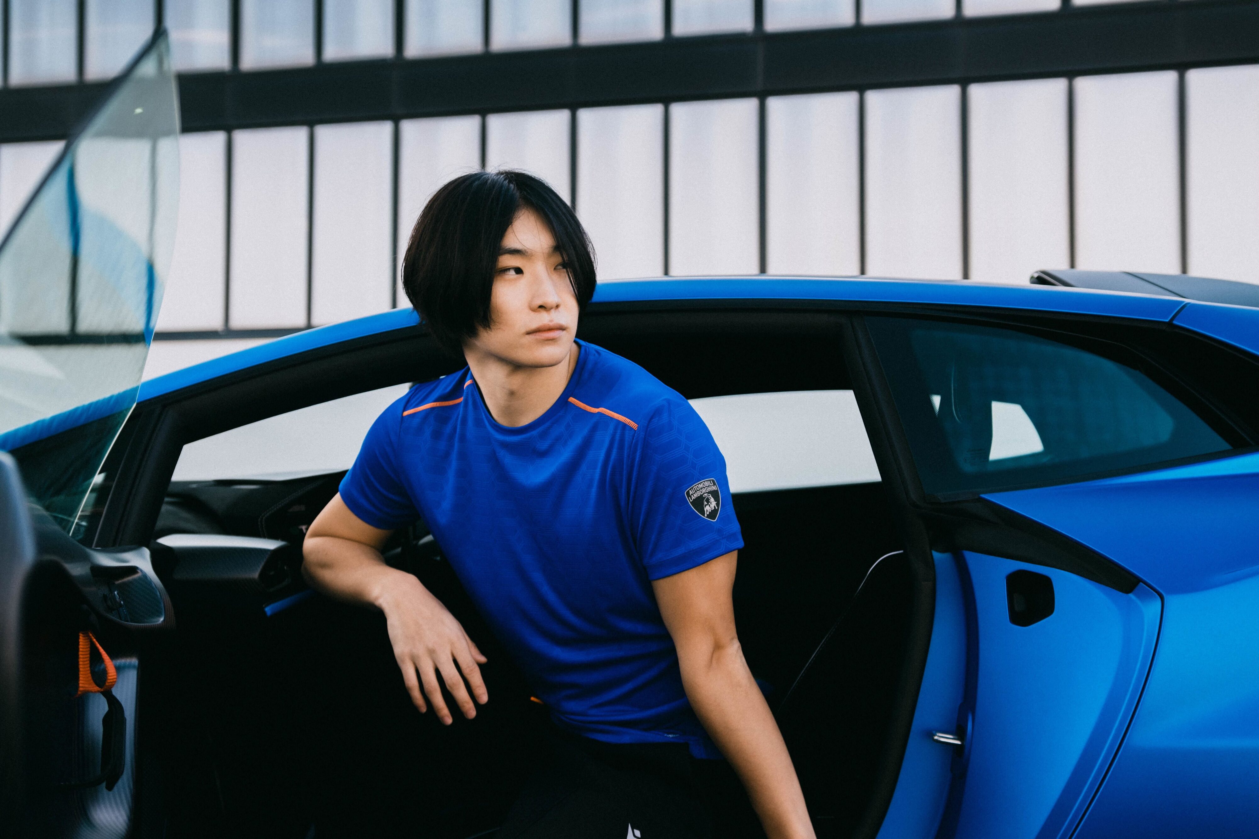 A model poses in a t-shirt from the Macron and Automobili Lamborghini Activewear range while sitting in a Lamborghini Huracan.
