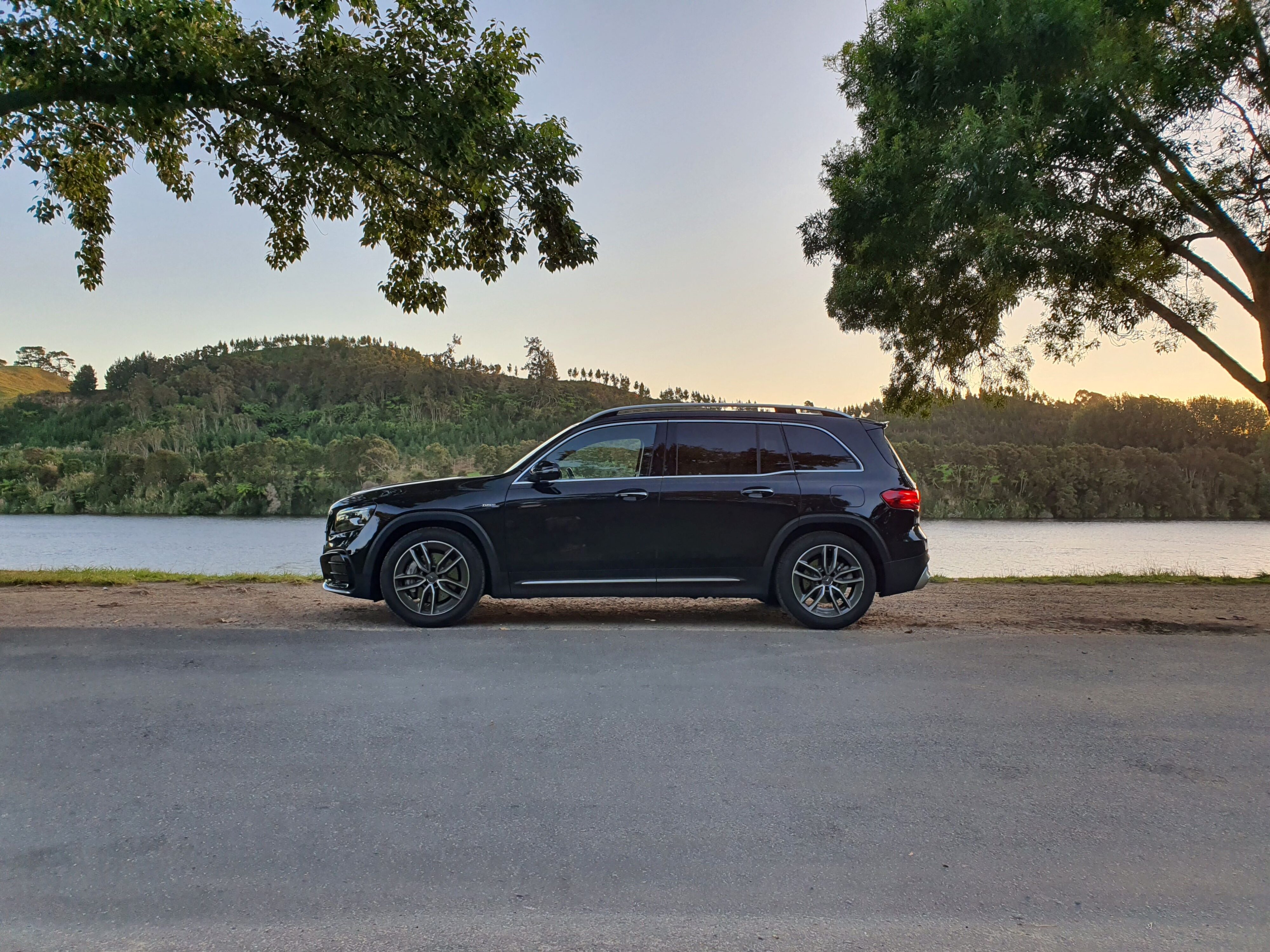 Side on view of a 2024 Mercedes-AMG GLB 35 4MATIC in Black with Lake Karapiro, Cambridge in the background.