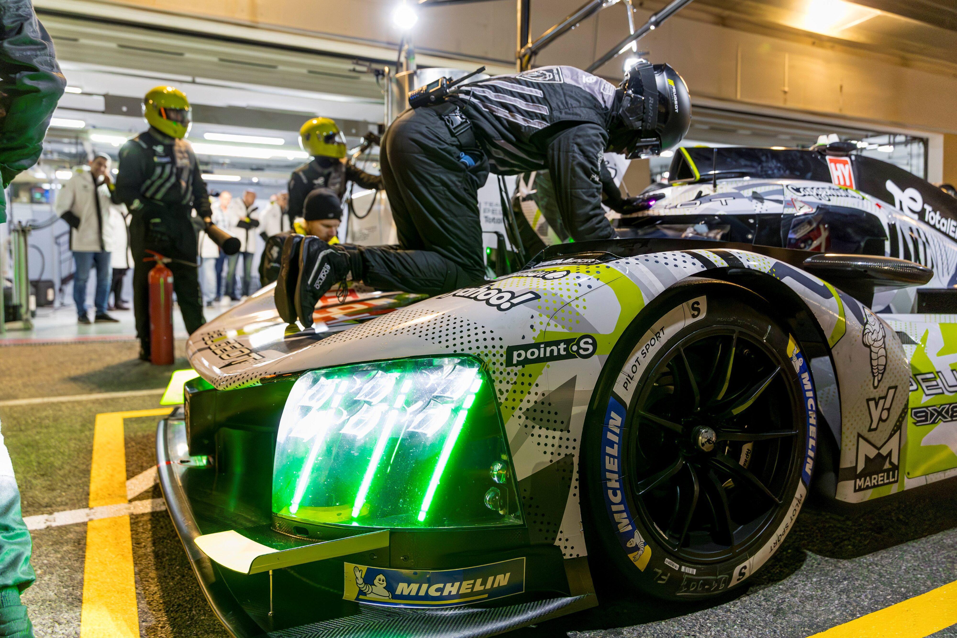 A photo of pit crew working on the Peugeot Sport 9X8 Hypercar with Point S sponsorship on the side.