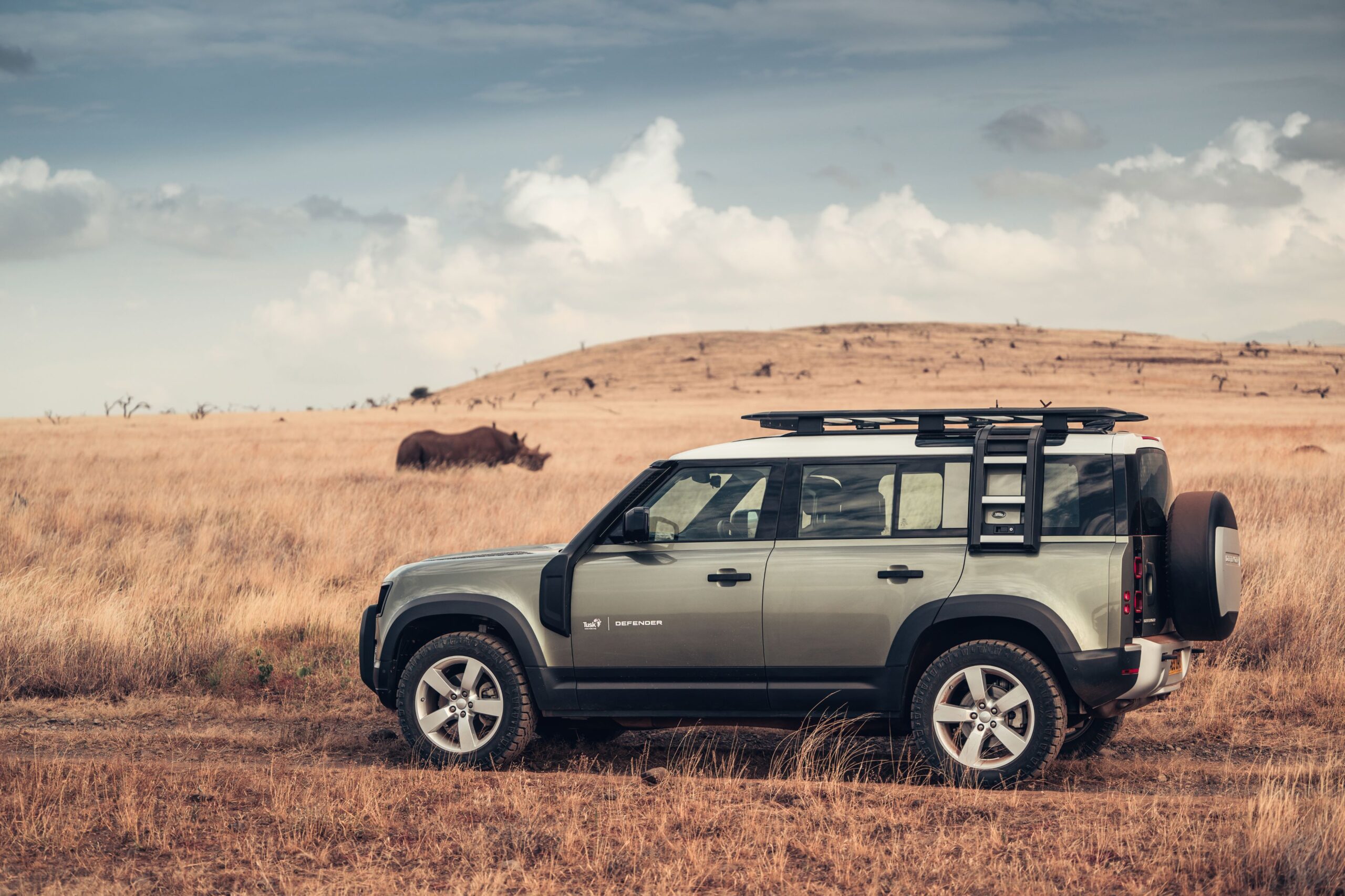 A Tusk branded Land Rover Defender 110 with a Rhinoceros in the background.