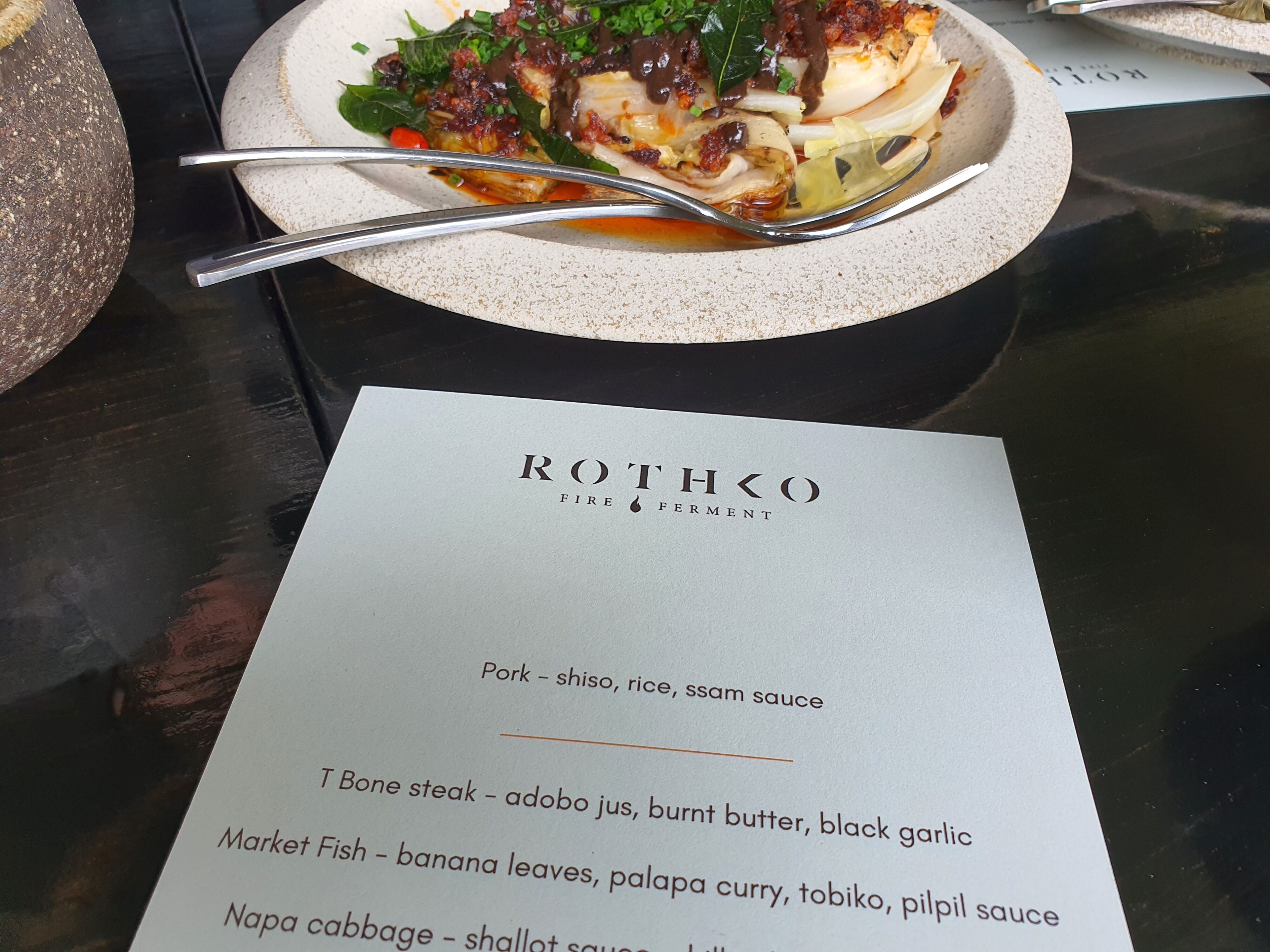 A photo of the menu at Sculptureum's Rothko Restaurant with a plate of food in the background.