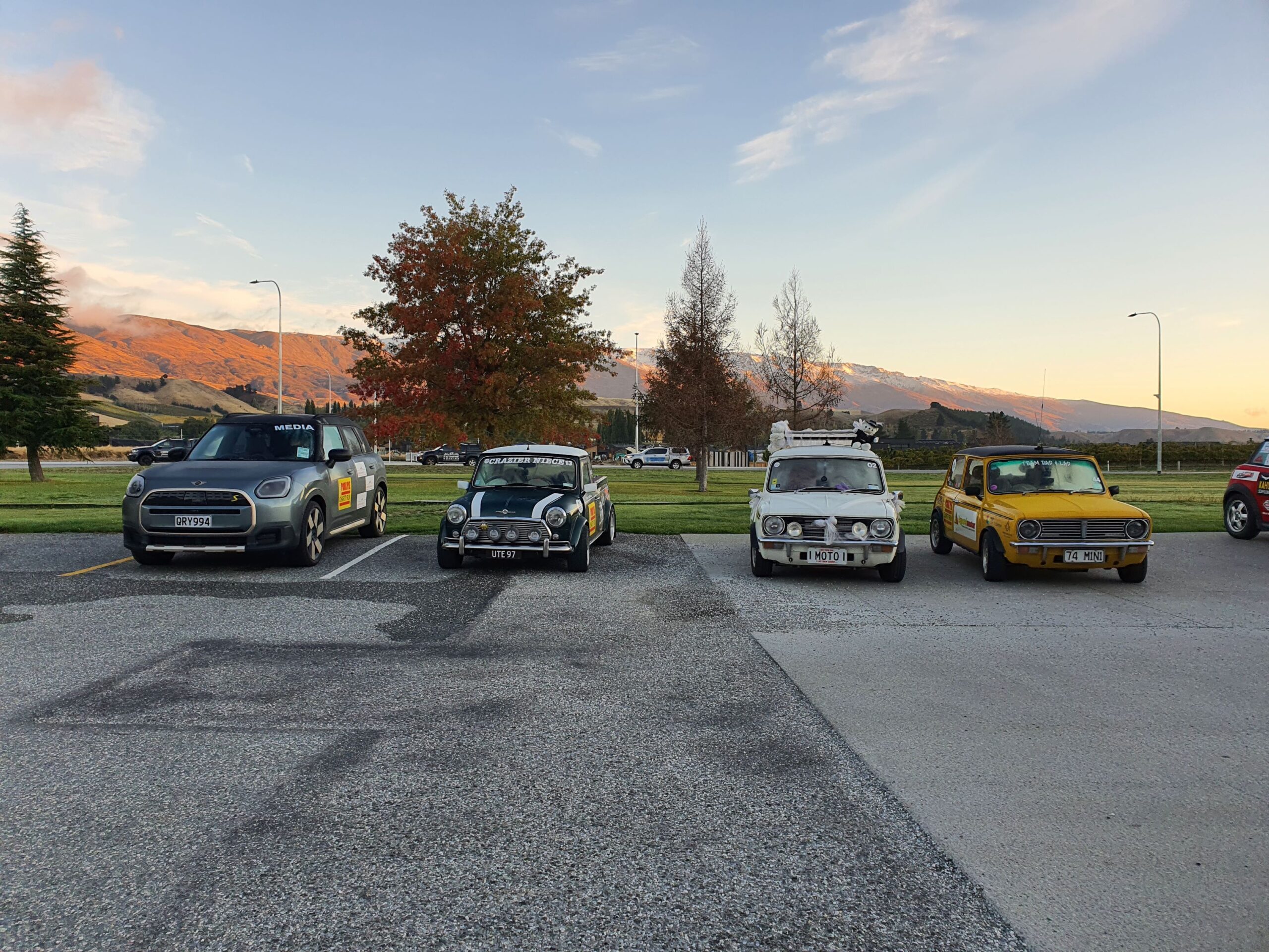 A 2025 Mini Countryman SE joined by three classic Minis with the 'The Remarkables' in the background as the sun rises over Cromwell on day six of the 2025 Pork Pie Charity Run.