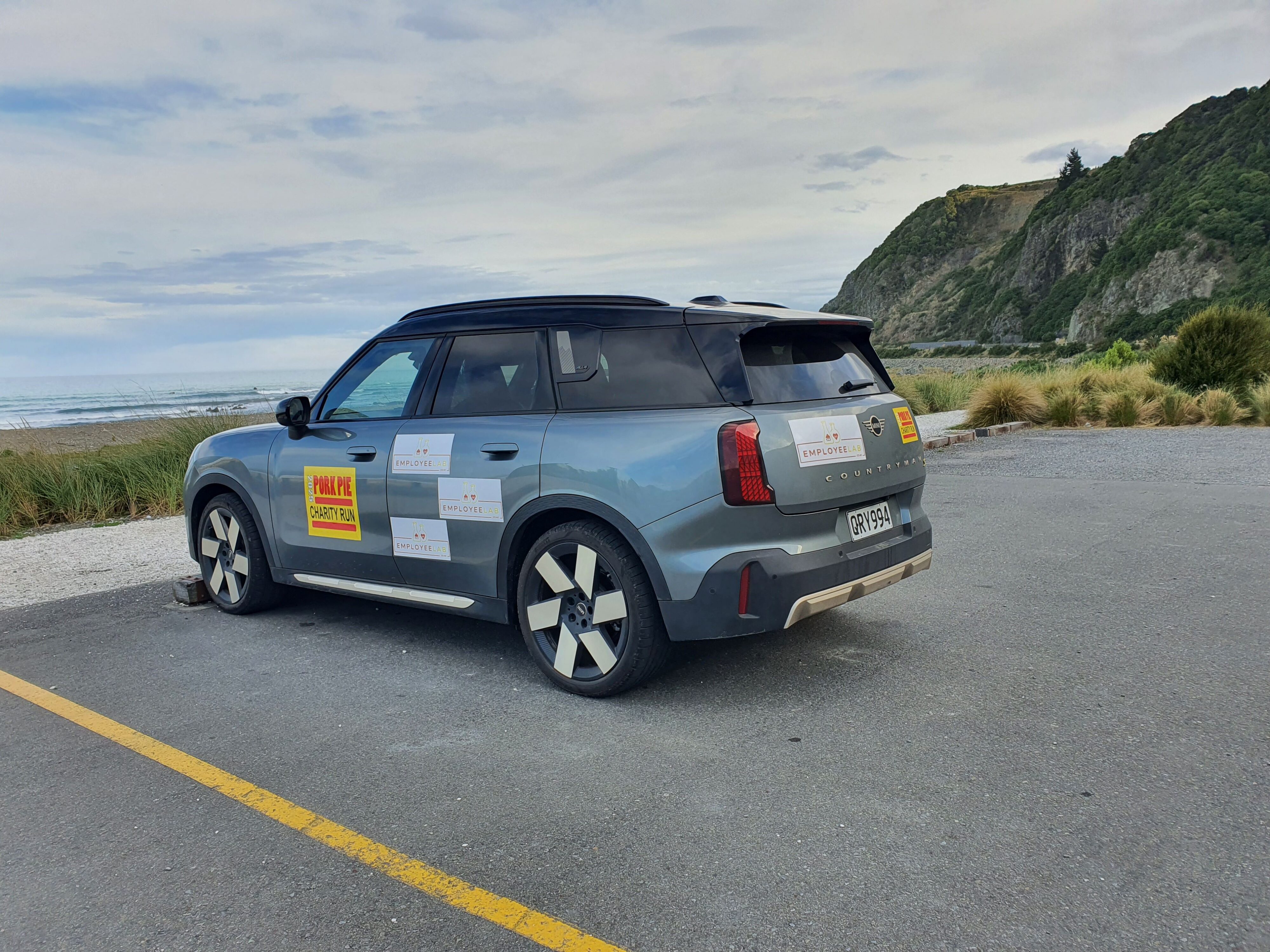 A 2025 Mini Countryman SE All4 with Employee Lab branding and ocean in the background, taken just outside Kaikoura on the 2025 Pork Pie Charity Run.