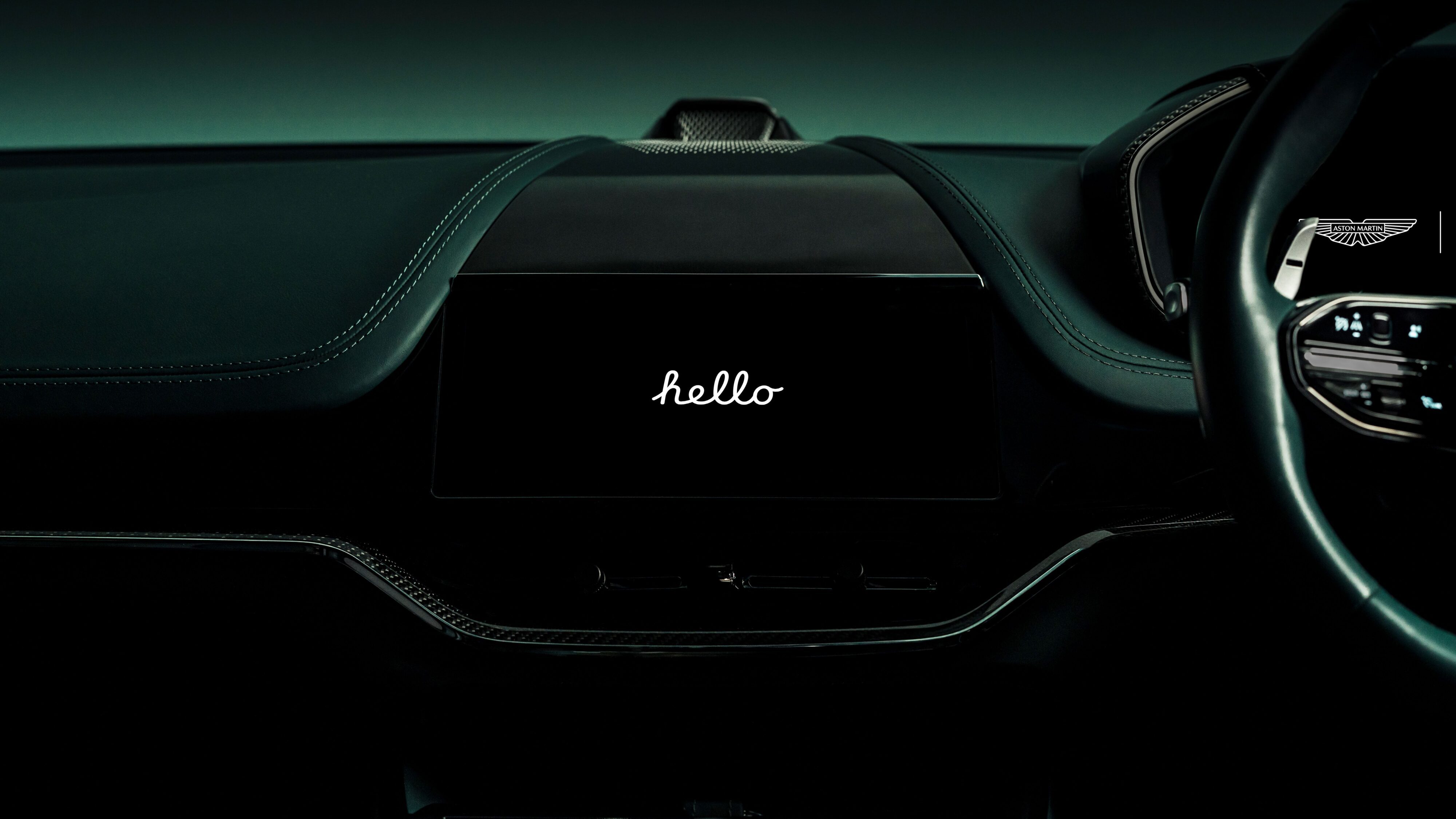 The infotainment screen of an Aston Martin DBX with Apple CarPlayUltra displaying the text 'hello' in a stylized font.