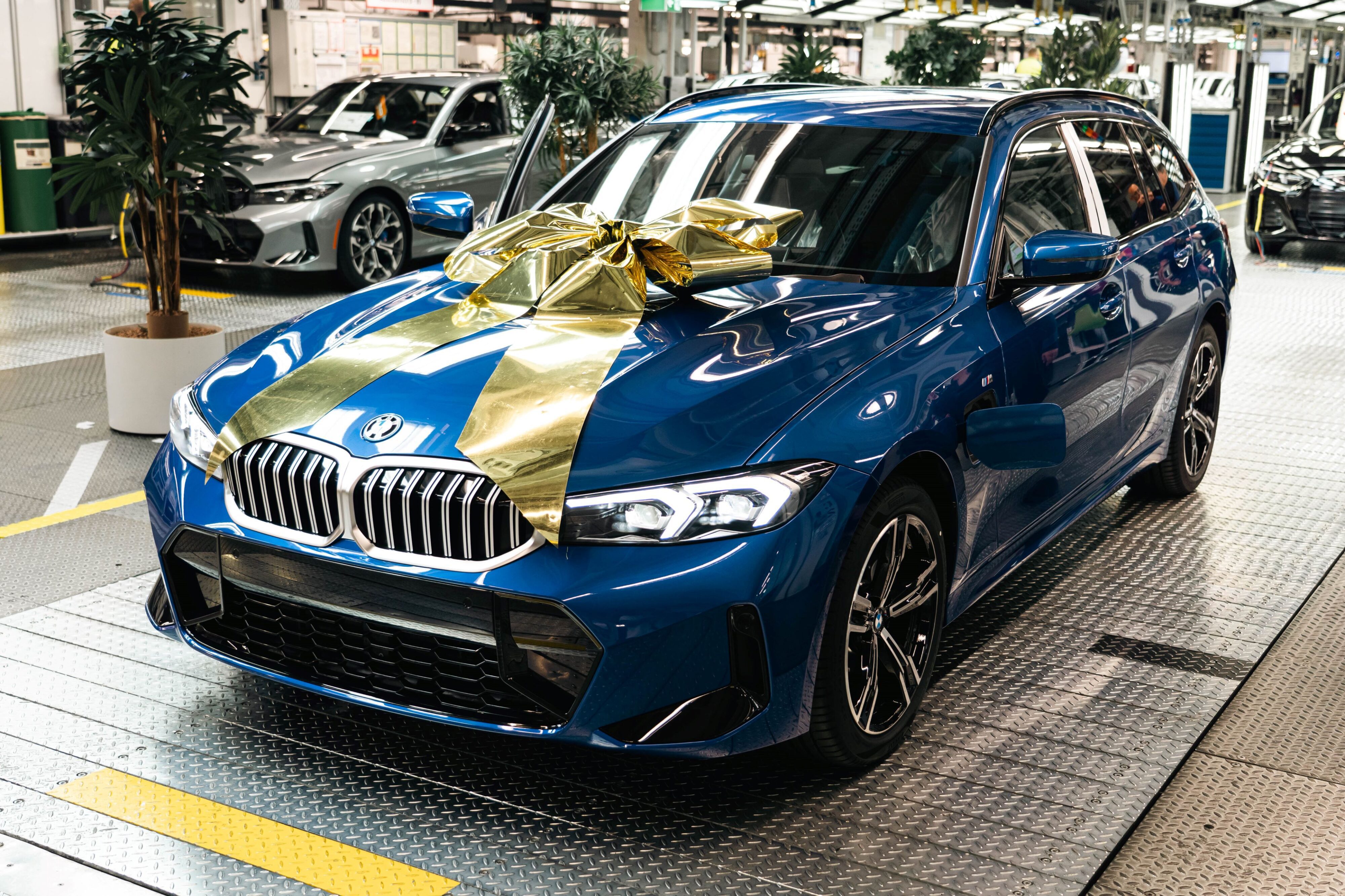 A photo of the three millionth BMW electrified vehicle, a 330e Touring in Portimao Blue with a gold ribbon on its bonnet to celebrate the occasion.