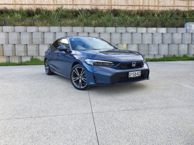 Front three quarters view of a 2025 Honda Civic e:hev in Ocean Blue Pearl with concrete in the background.