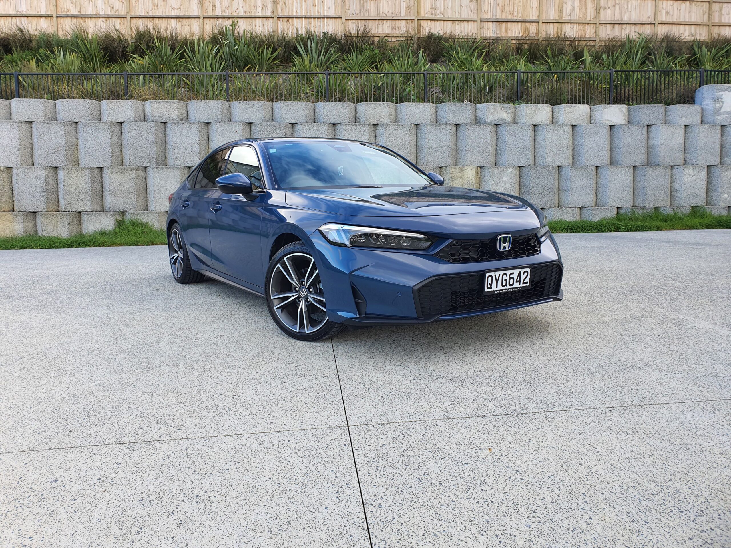 Front three quarters view of a 2025 Honda Civic e:hev in Ocean Blue Pearl with concrete in the background.