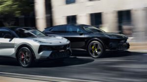 A photo of two Lotus Eletre hyper electric SUVs side by side in motion. One in white and one in black.