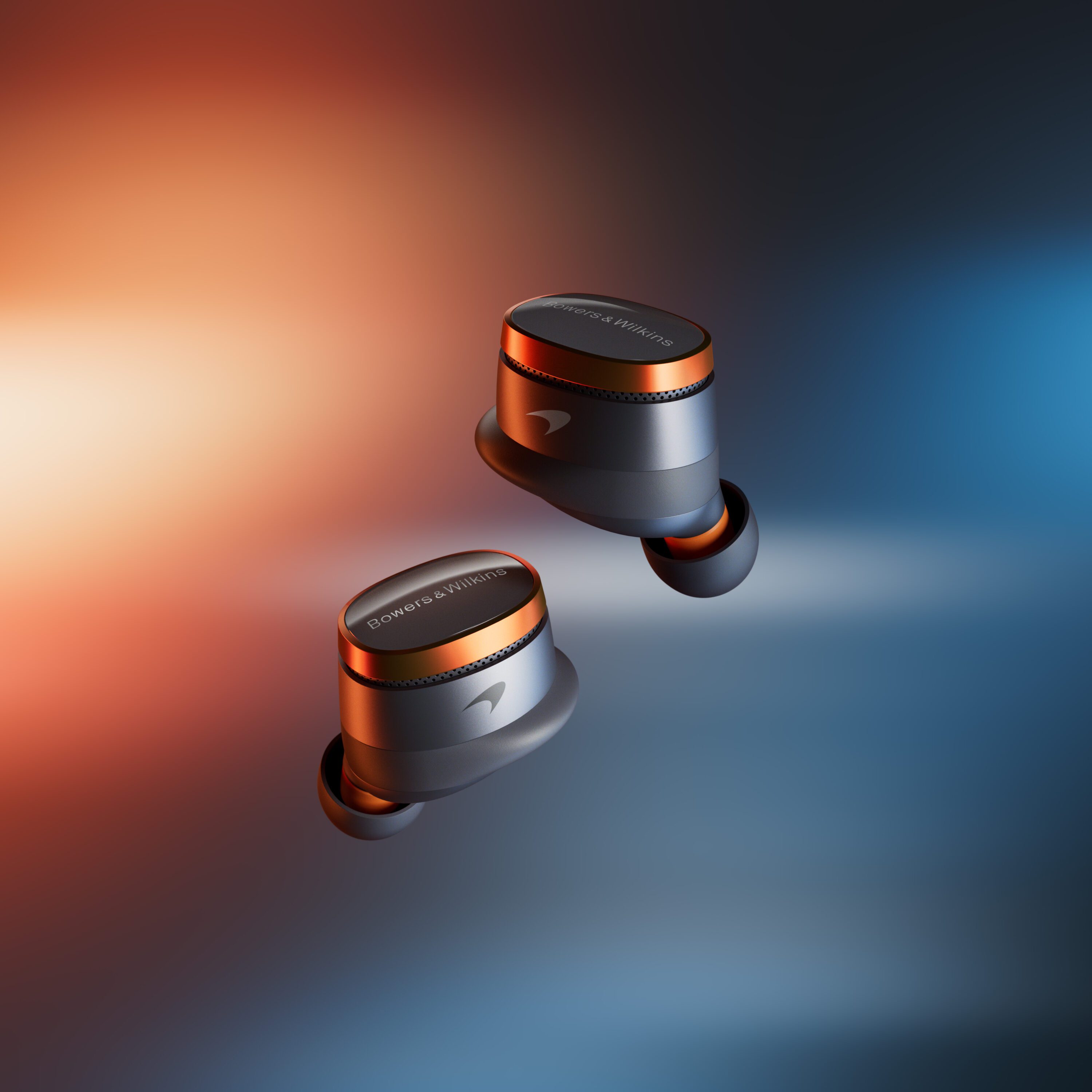 A photo of the Bowers & Wilkins Pi8 McLaren Edition earbuds in Galvanic Grey & Papaya Orange.