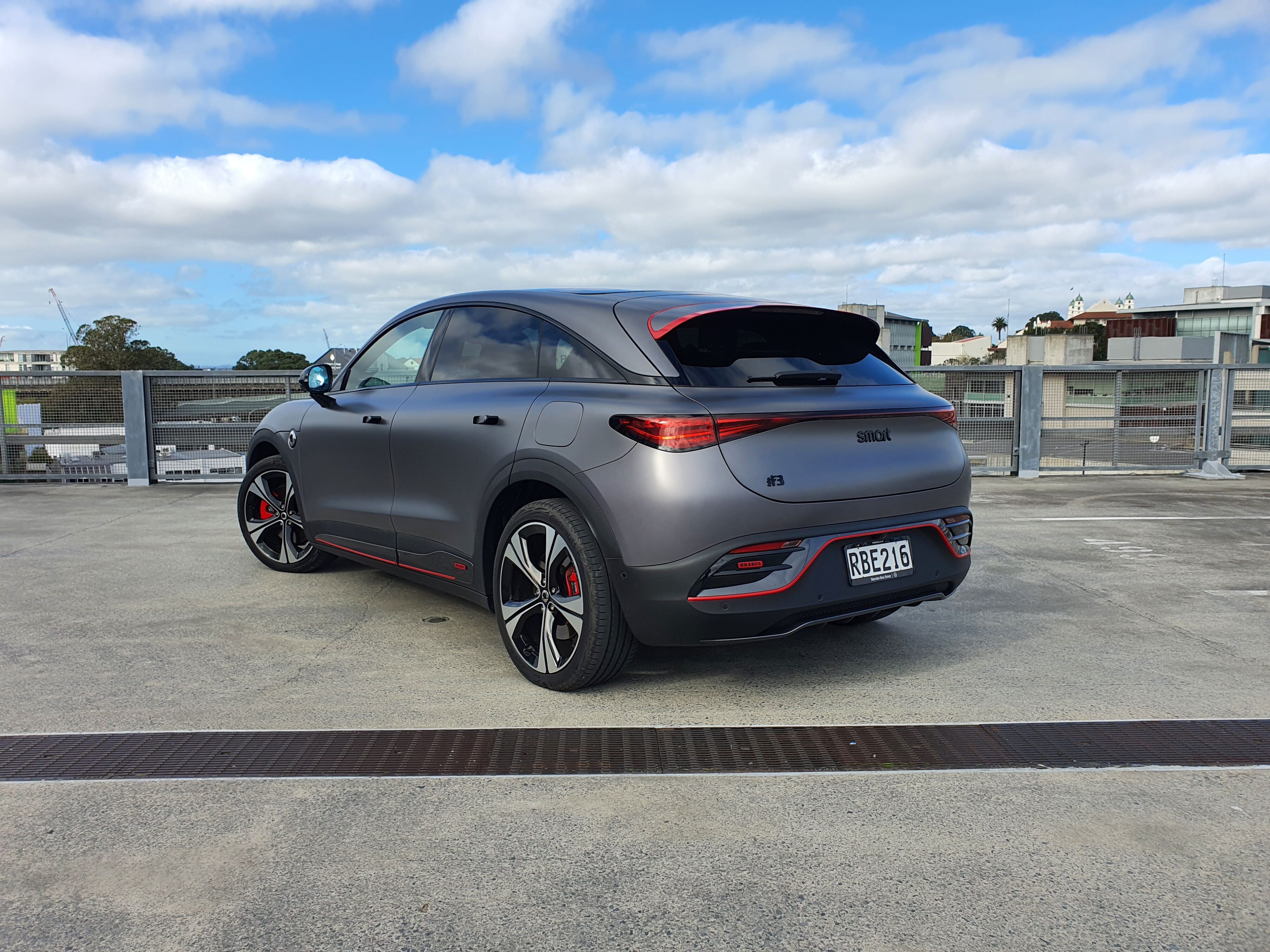 Rear three quarters view of a matte grey 2025 smart #3 Brabus photographed atop a parking building in Auckland.