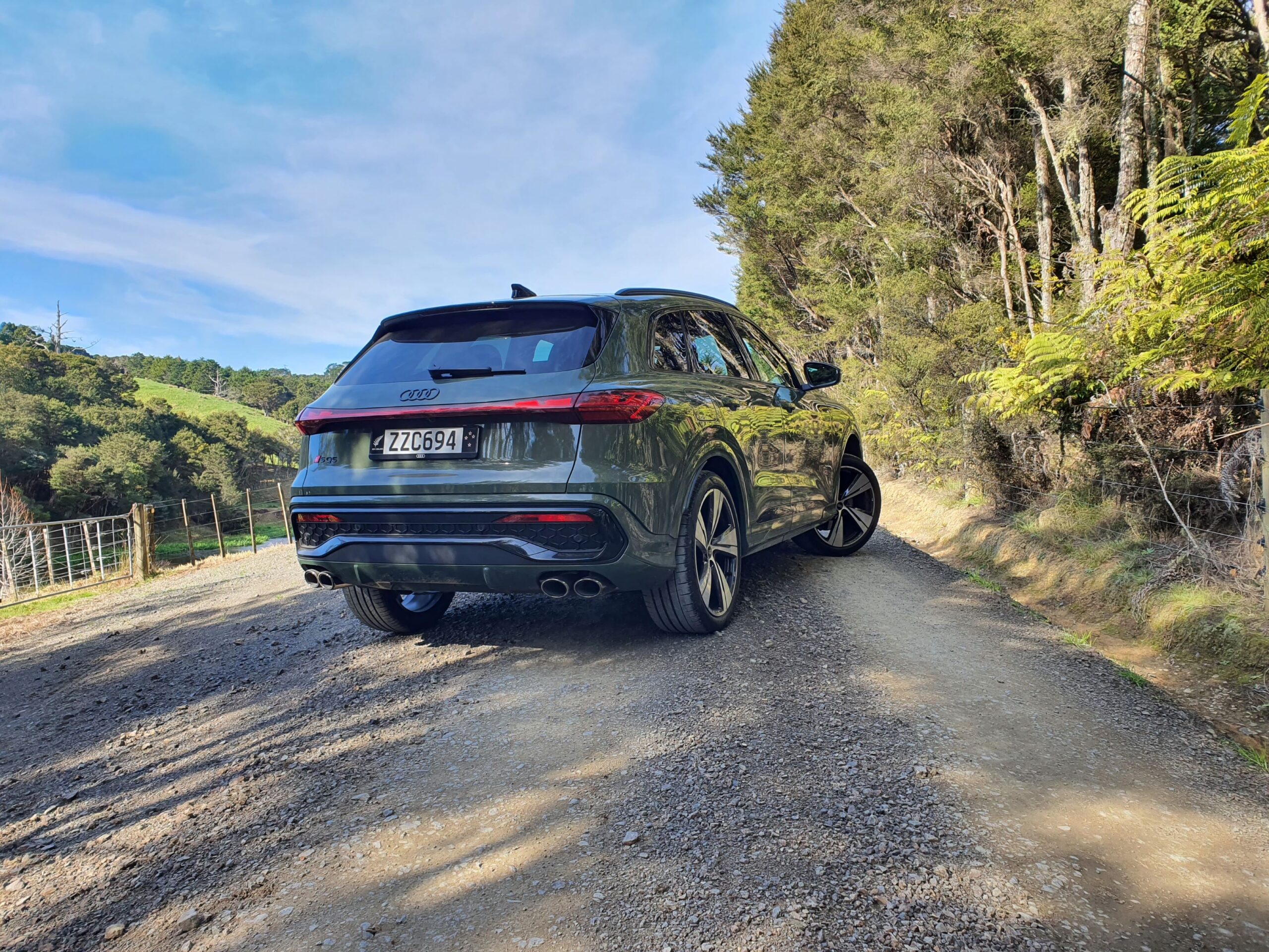 Rear three quarters view of a 2025 Audi SQ5 in District Green, taken at Kauri Bay, Auckland.