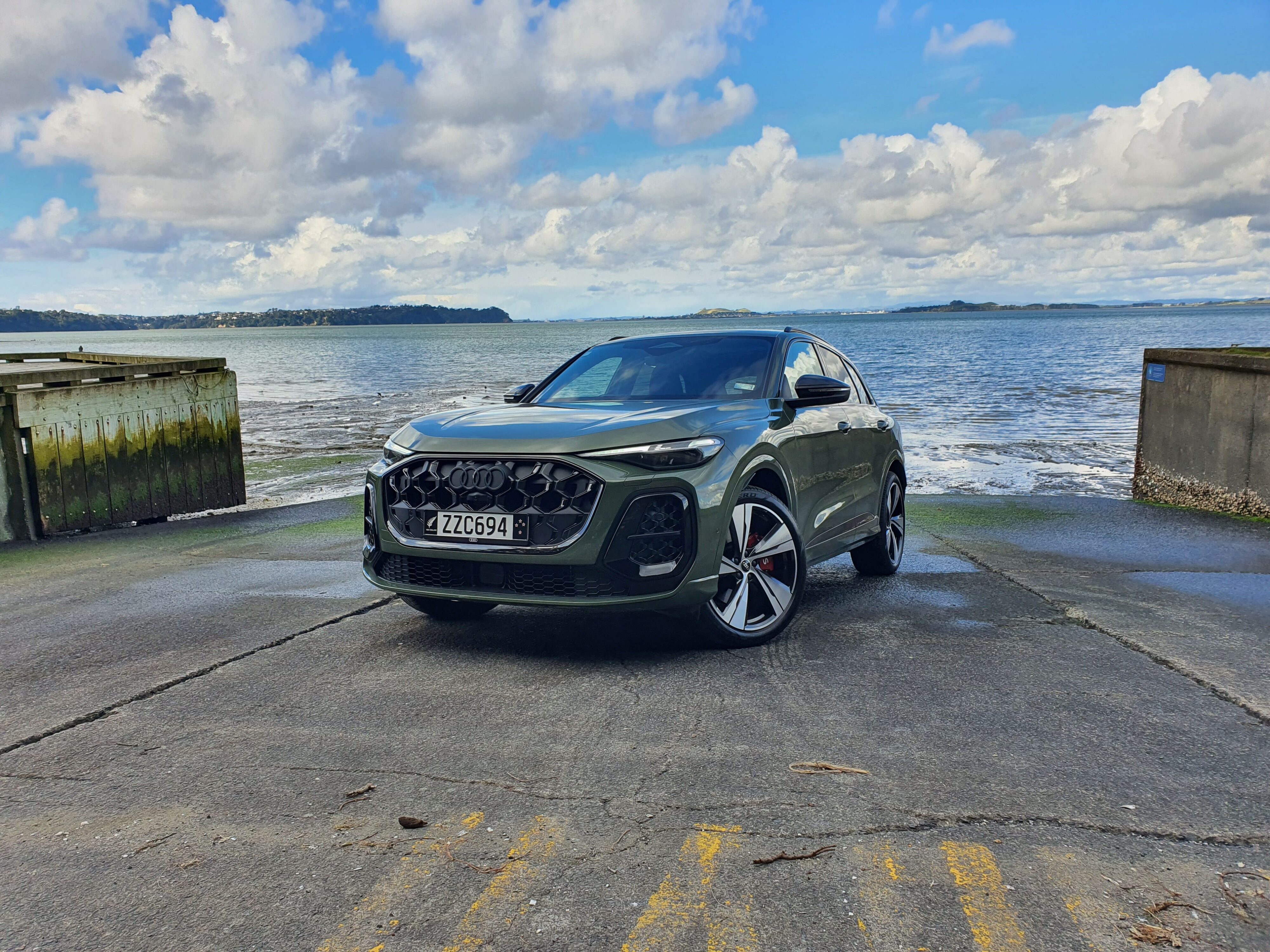 Front three quarters view of a 2025 Audi SQ5 in District Green with the ocean in the background.