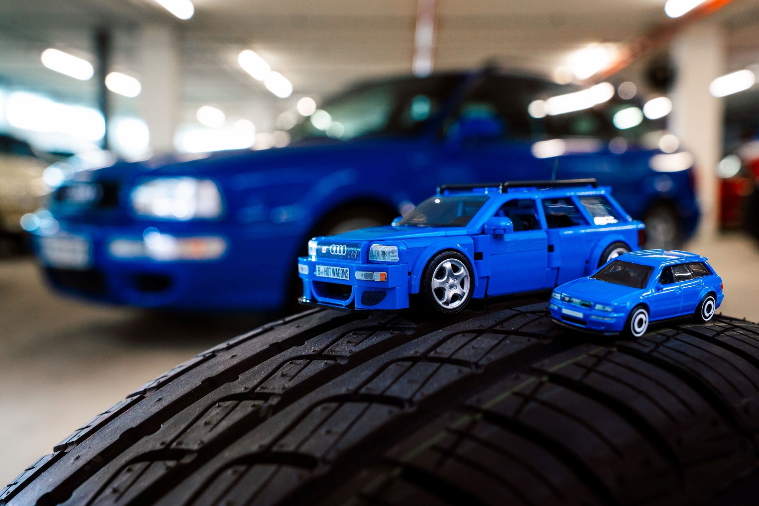 A photo depicting an Audi RS2 Avant in Nogaro Blue as a Hot Wheels model, Mattel Brick Shop model and as a 1:1 scale vehicle.