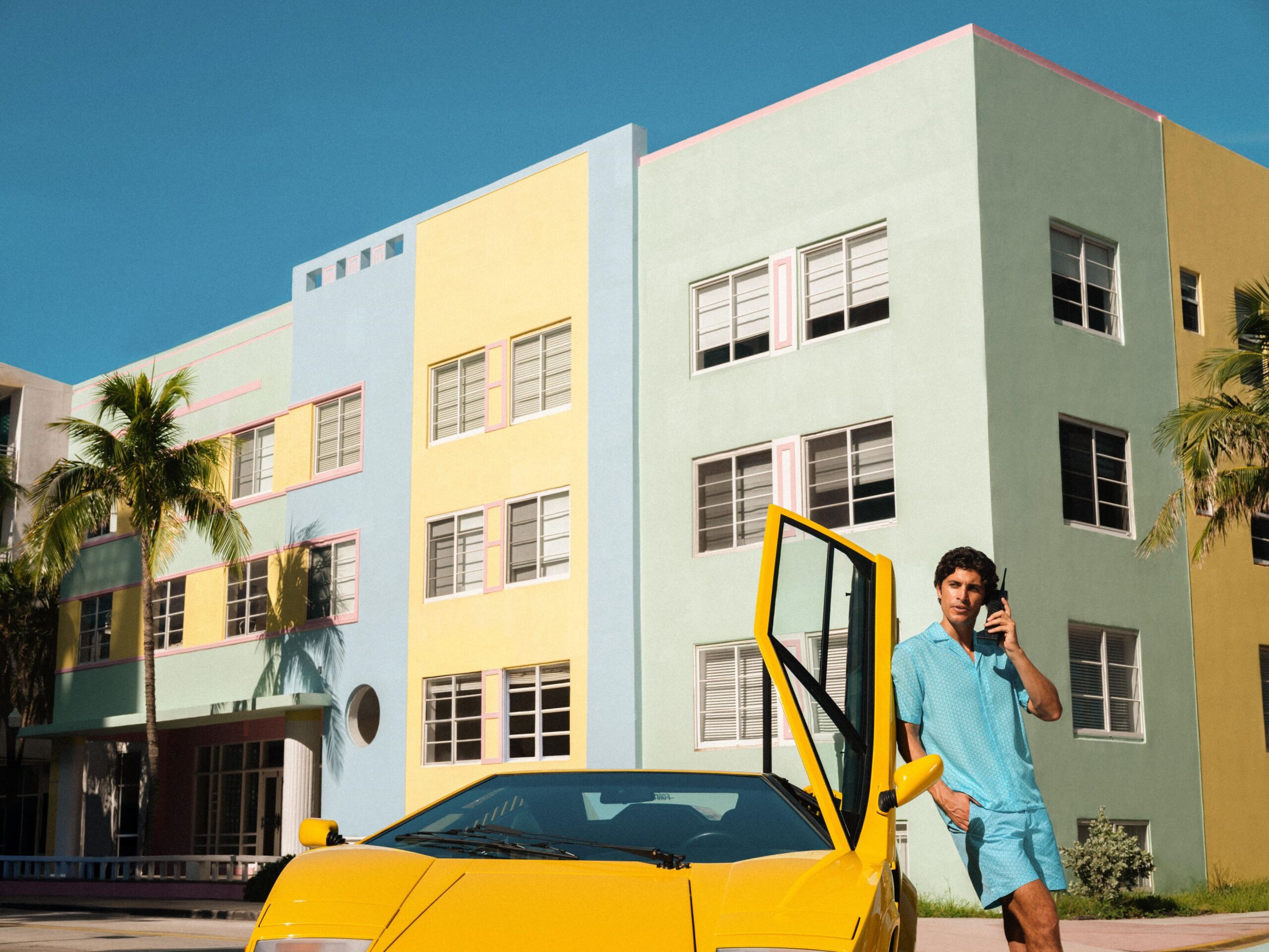 A photo of a model wearing the Orlebar Brown x Lamborghini collection posing next to a classic yellow Lamborghini Countach.
