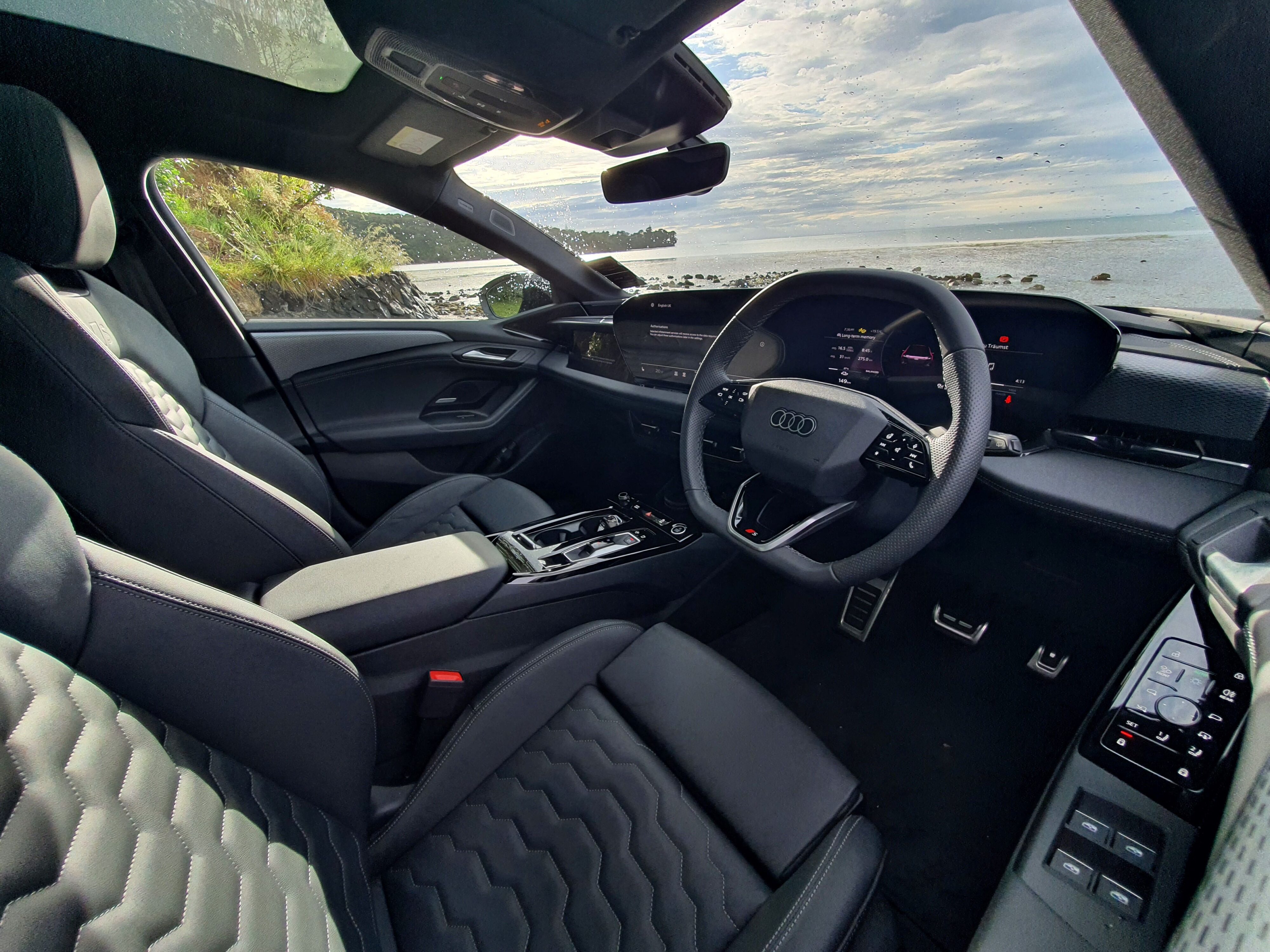 Interior view of the dashboard in an Audi A6 Avant e-tron S-Line quattro in Siam Beige with the ocean visible through the windscreen.