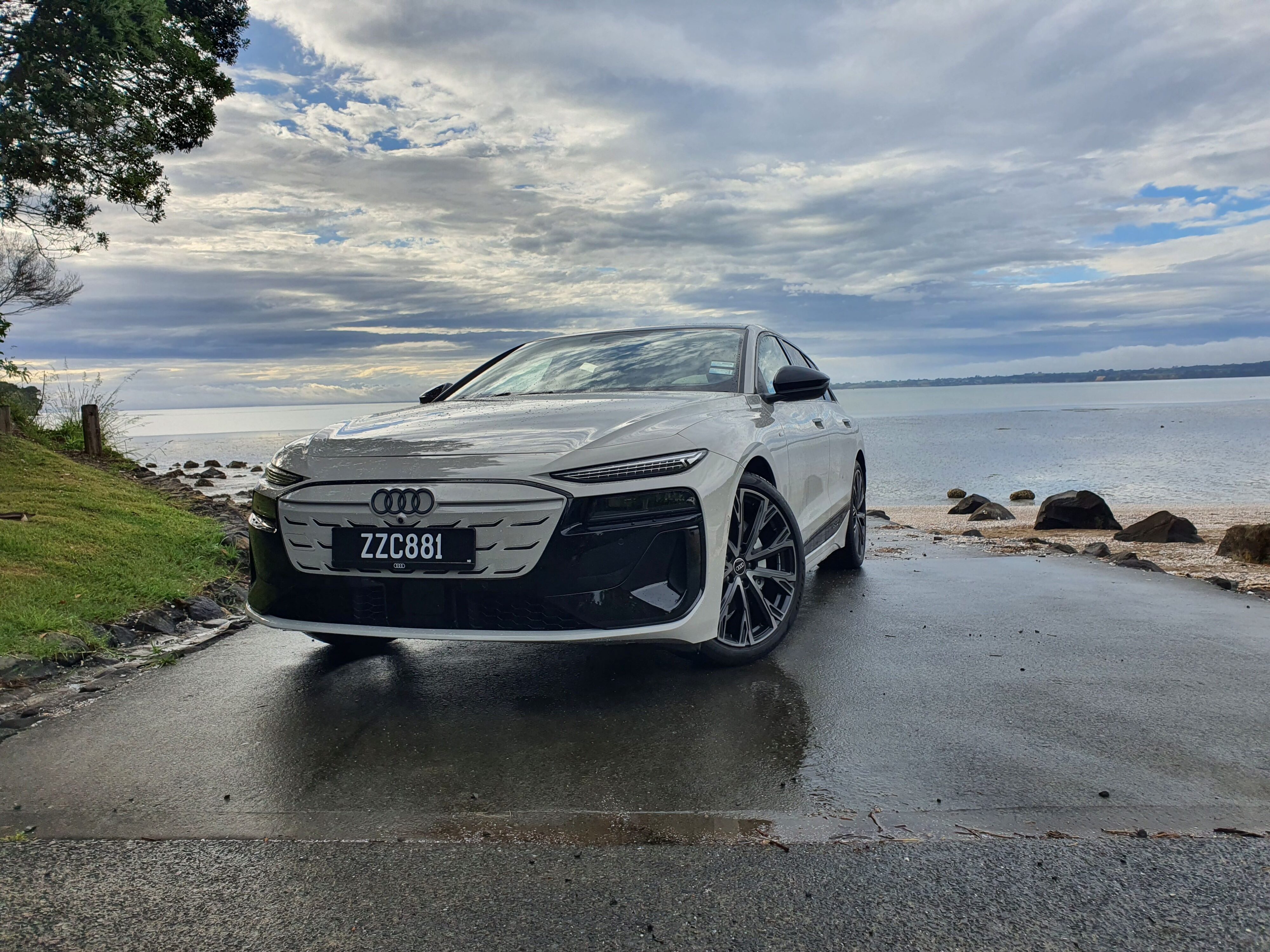 Front three quarters view of an Audi A6 Avant e-tron S-Line quattro in Siam Beige with the ocean in the background.