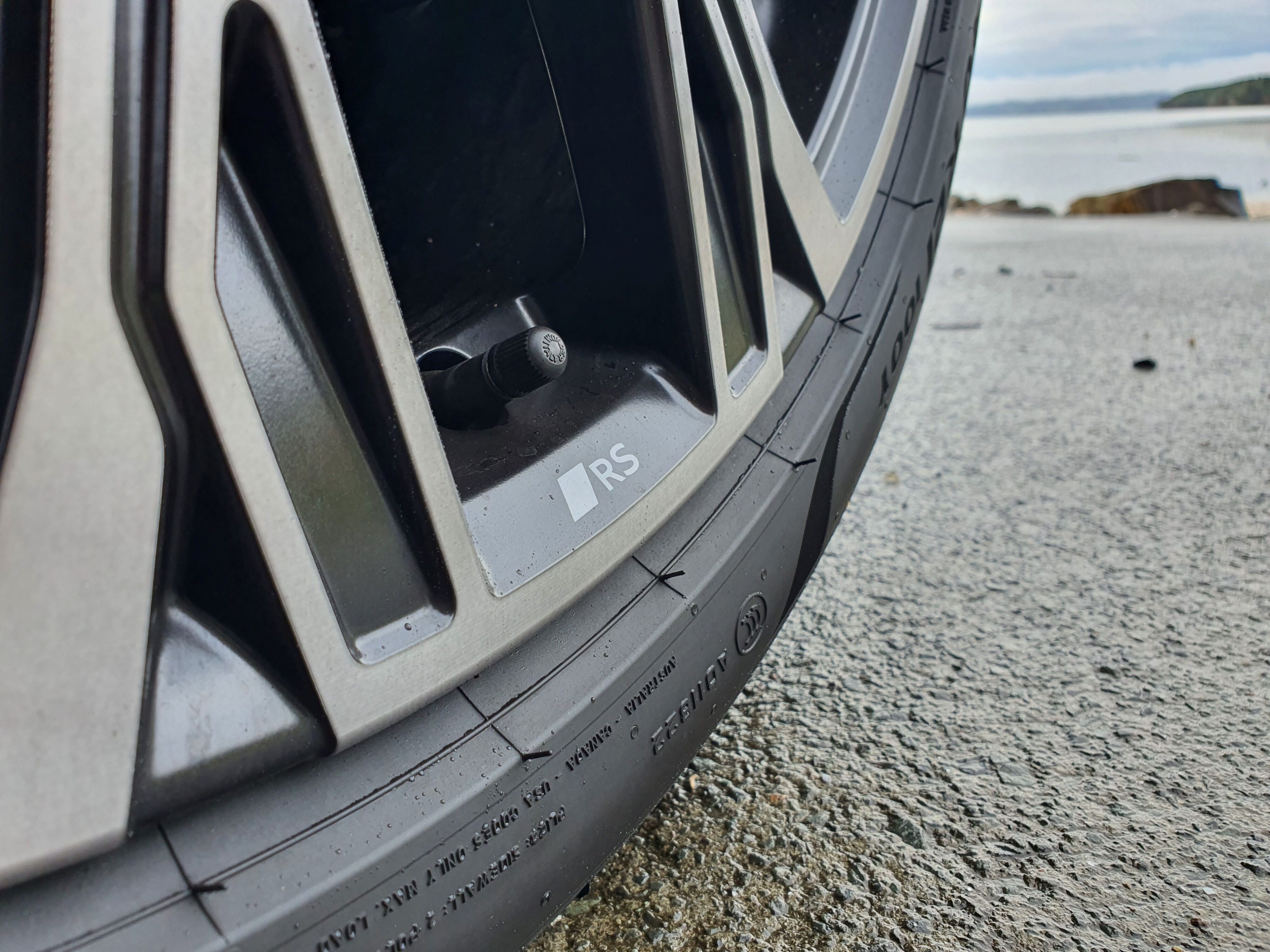 RS badging on the wheel of an Audi A6 Avant e-tron S-Line quattro in Siam Beige with the ocean in the background.