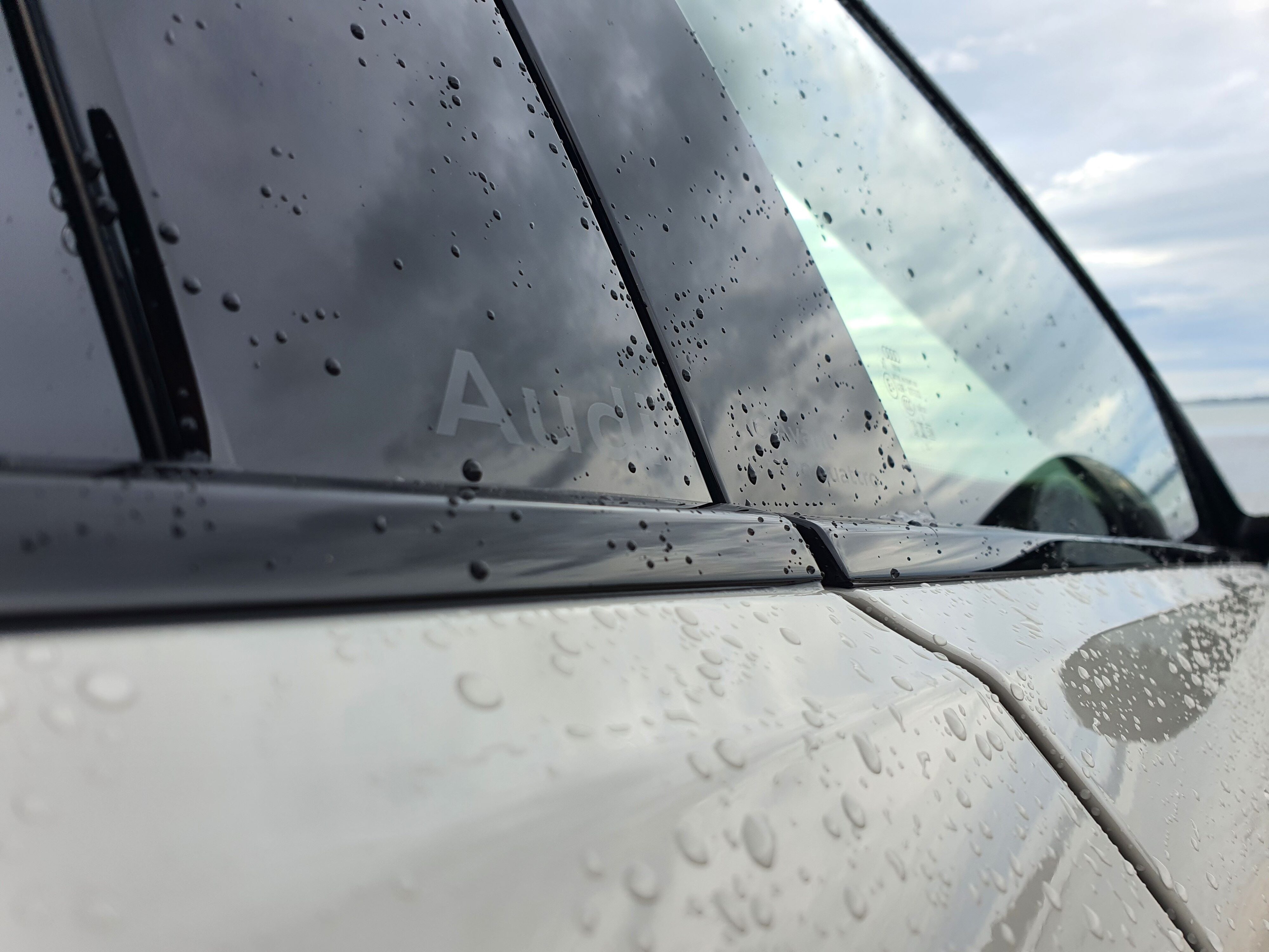A6 badging on the door pillar of an Audi A6 Avant e-tron S-Line quattro in Siam Beige with the ocean in the background.