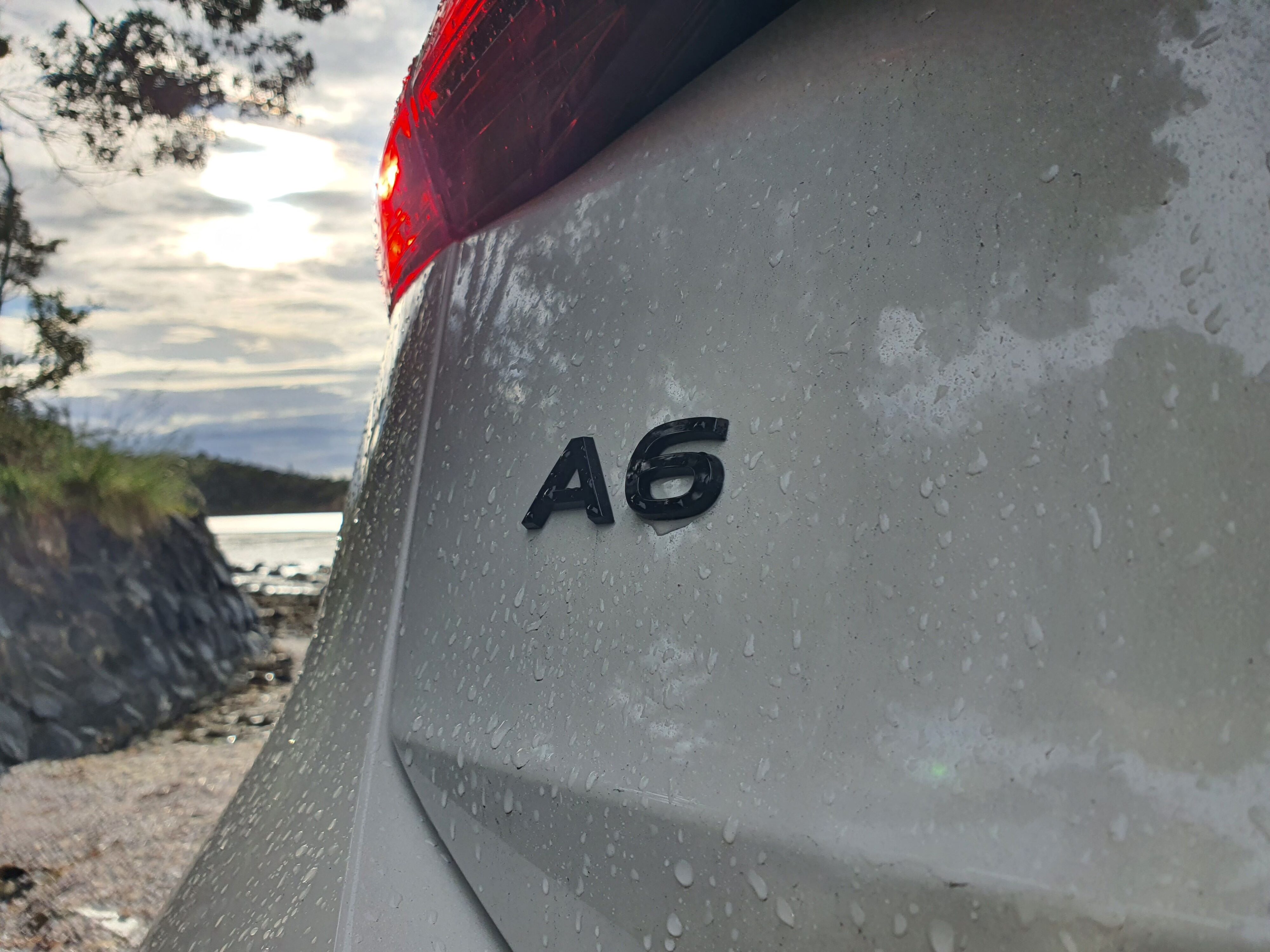 Quattro badging on the rear of an Audi A6 Avant e-tron S-Line quattro in Siam Beige with the ocean in the background.