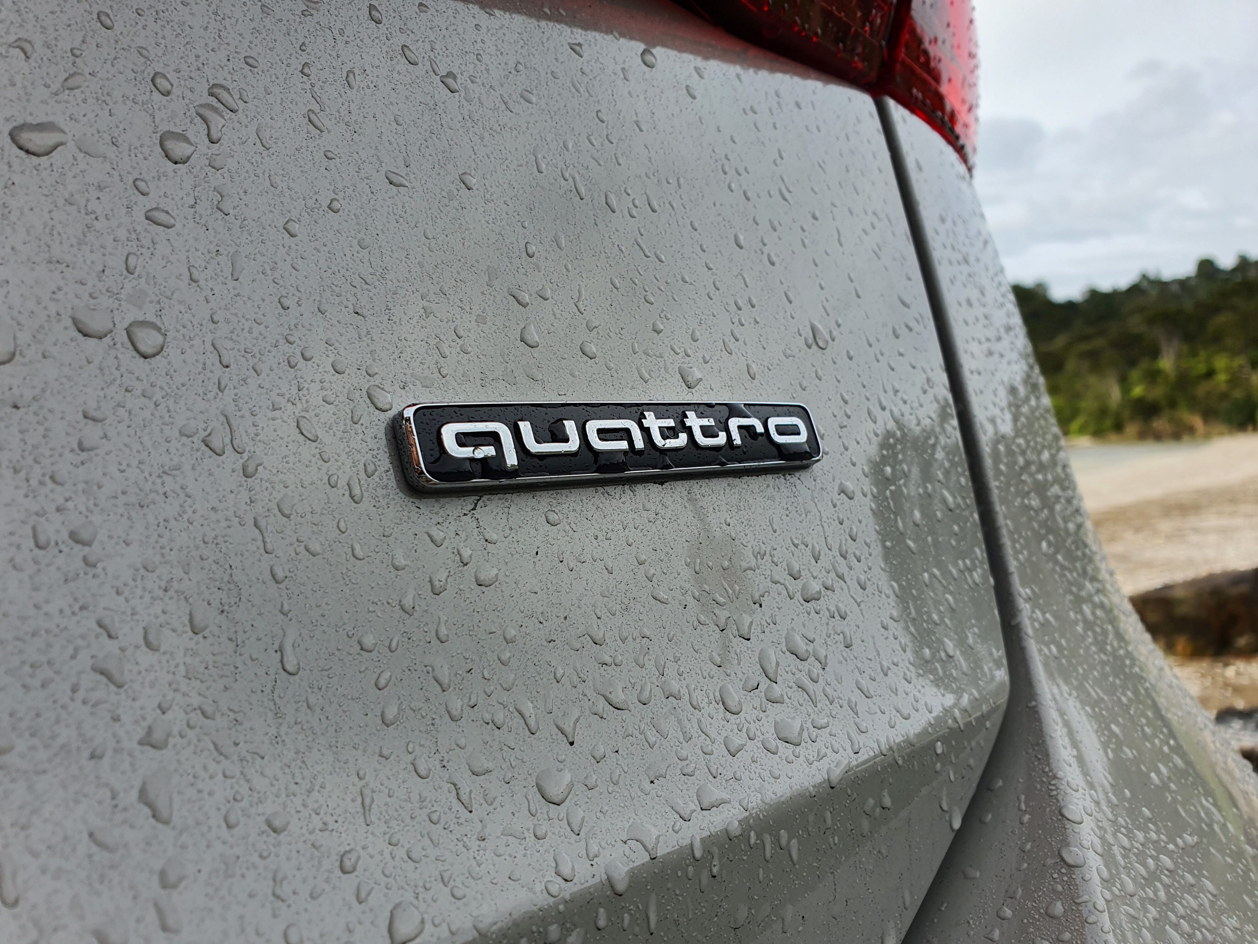 Quattro badging on the rear of an Audi A6 Avant e-tron S-Line quattro in Siam Beige with the ocean in the background.