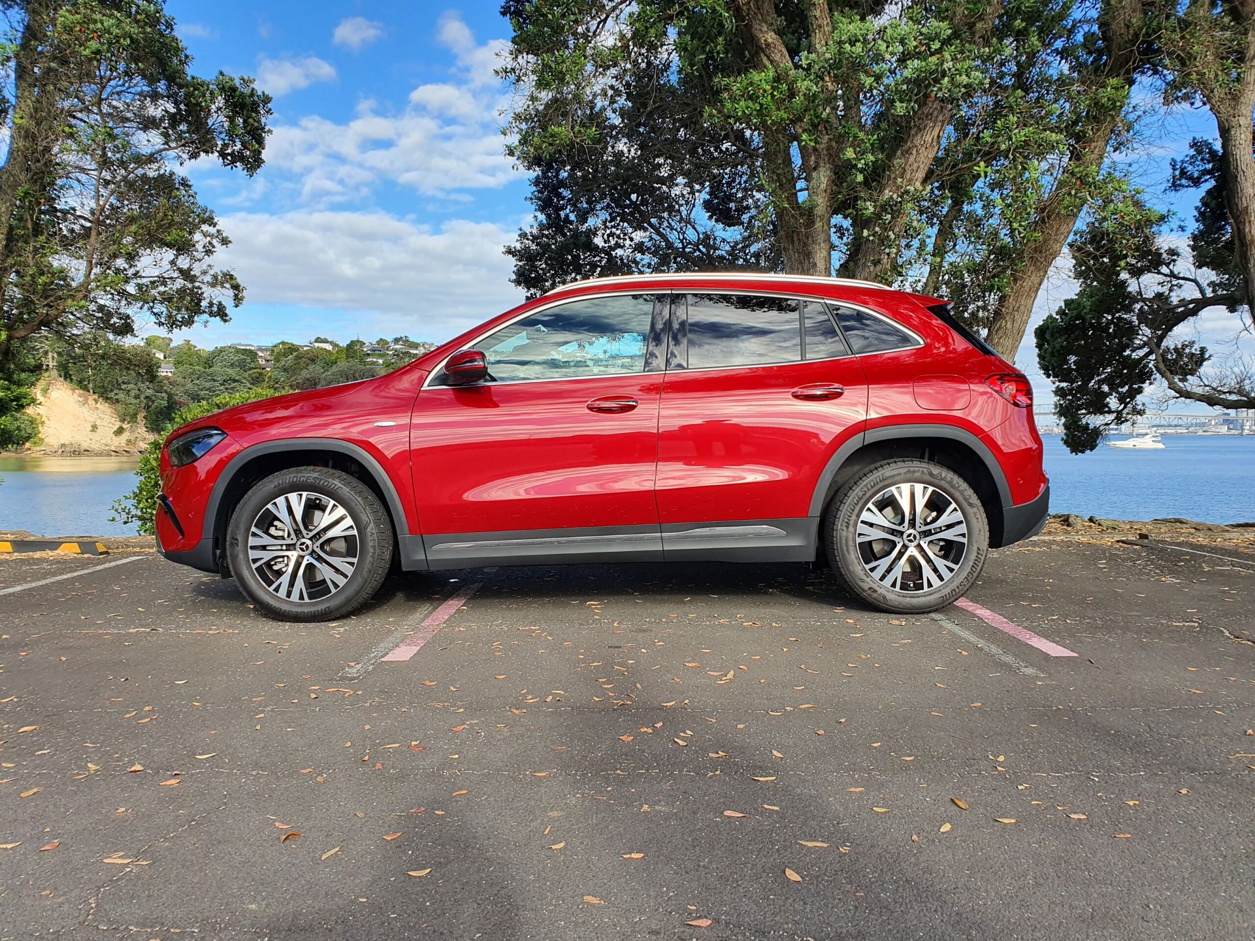 Side on view of a 2025 Mercedes-Benz GLA250e in Patagonia Red Metallic with the ocean in the background.