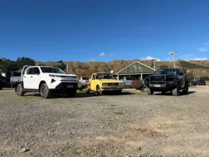 Photograph of a 1977 yellow Toyota Hilux in between a white 2026 Toyota Hilux SR BEV and a 2026 Toyota Hilux SR at the New Zealand launch of the 2026 ninth-generation Toyota Hilux, taken at Heights Experience in Manawatu, New Zealand.