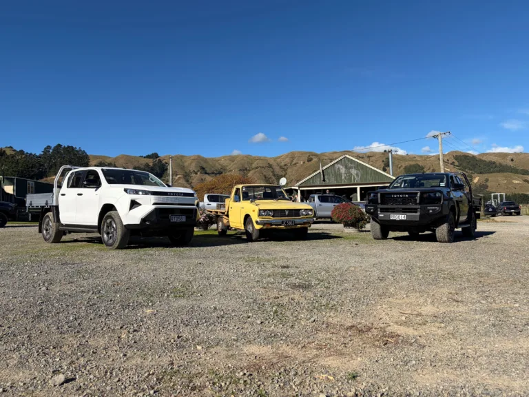 Photograph of a 1977 yellow Toyota Hilux in between a white 2026 Toyota Hilux SR BEV and a 2026 Toyota Hilux SR at the New Zealand launch of the 2026 ninth-generation Toyota Hilux, taken at Heights Experience in Manawatu, New Zealand.