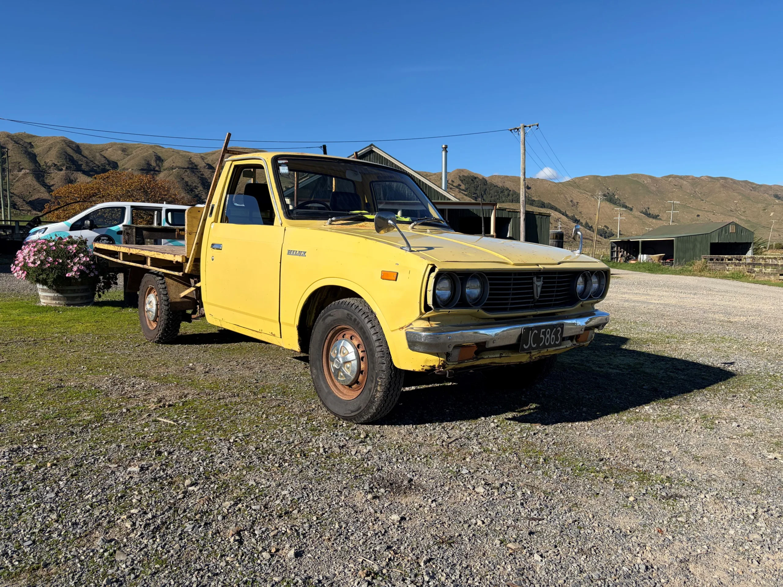 Photograph of the front three quarters of a 1977 Toyota Hilux in yellow at the New Zealand launch of the 2026 ninth-generation Toyota Hilux, taken at Heights Experience in Manawatu, New Zealand.