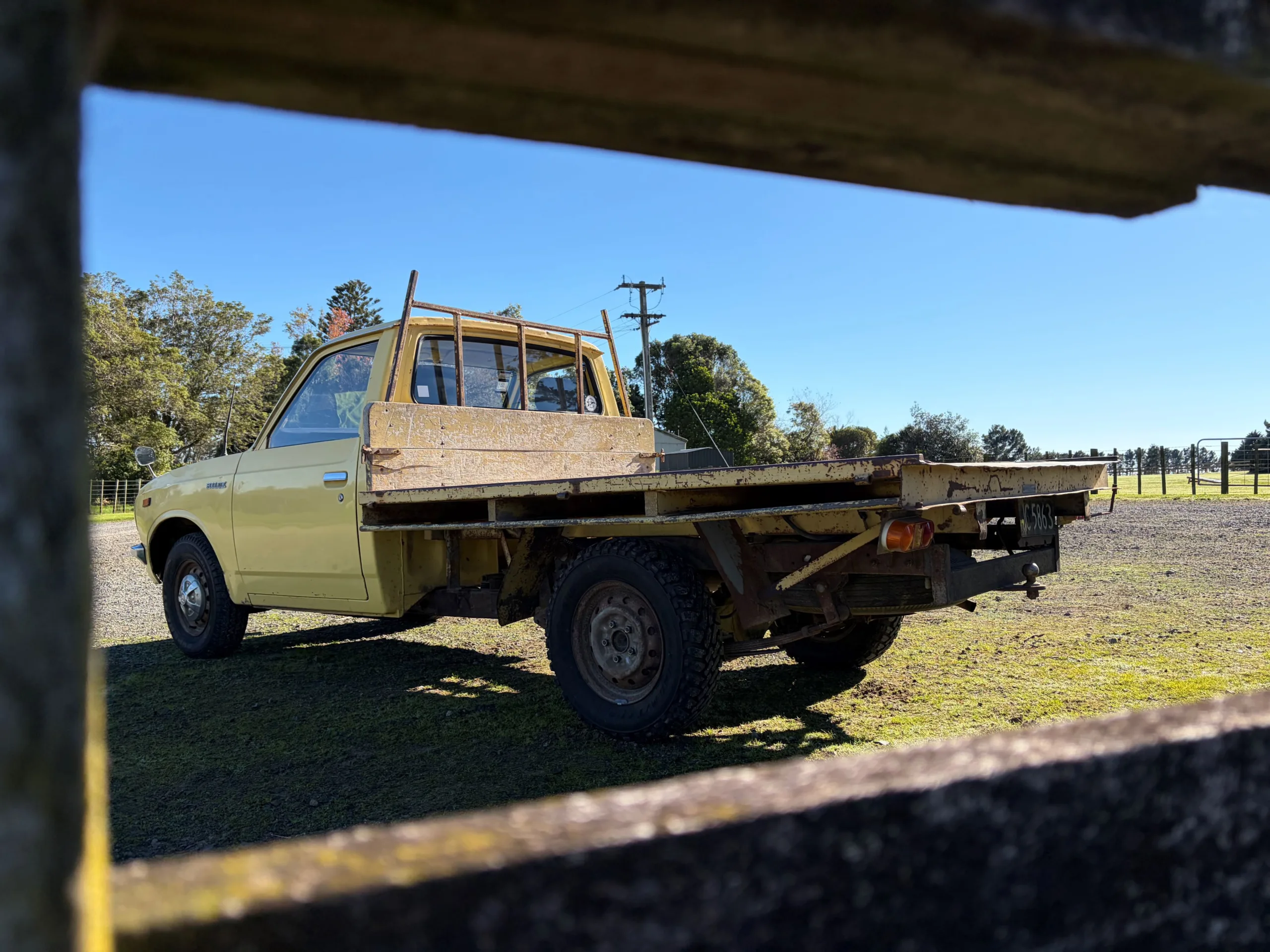 Photograph of the rear three quarters of a 1977 Toyota Hilux in yellow at the New Zealand launch of the 2026 ninth-generation Toyota Hilux, taken at Heights Experience in Manawatu, New Zealand.