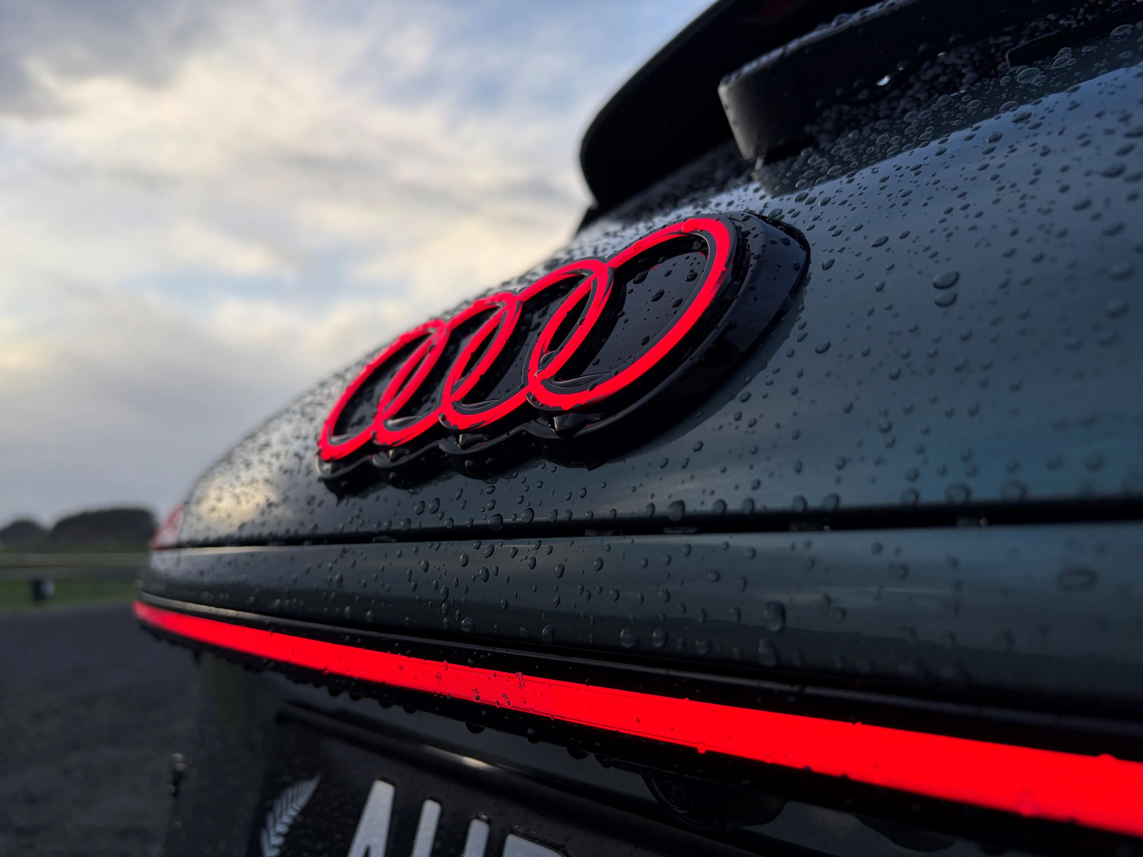 Close up of the Audi logo on the rear of a 2026 Audi Q3 195kW S-Line quattro in Sage Green, photographed at sunset.
