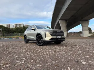 Front three quarters view of a 2026 GWM Haval H6 HEV in Astral Pearl, photographed against an urban backdrop.