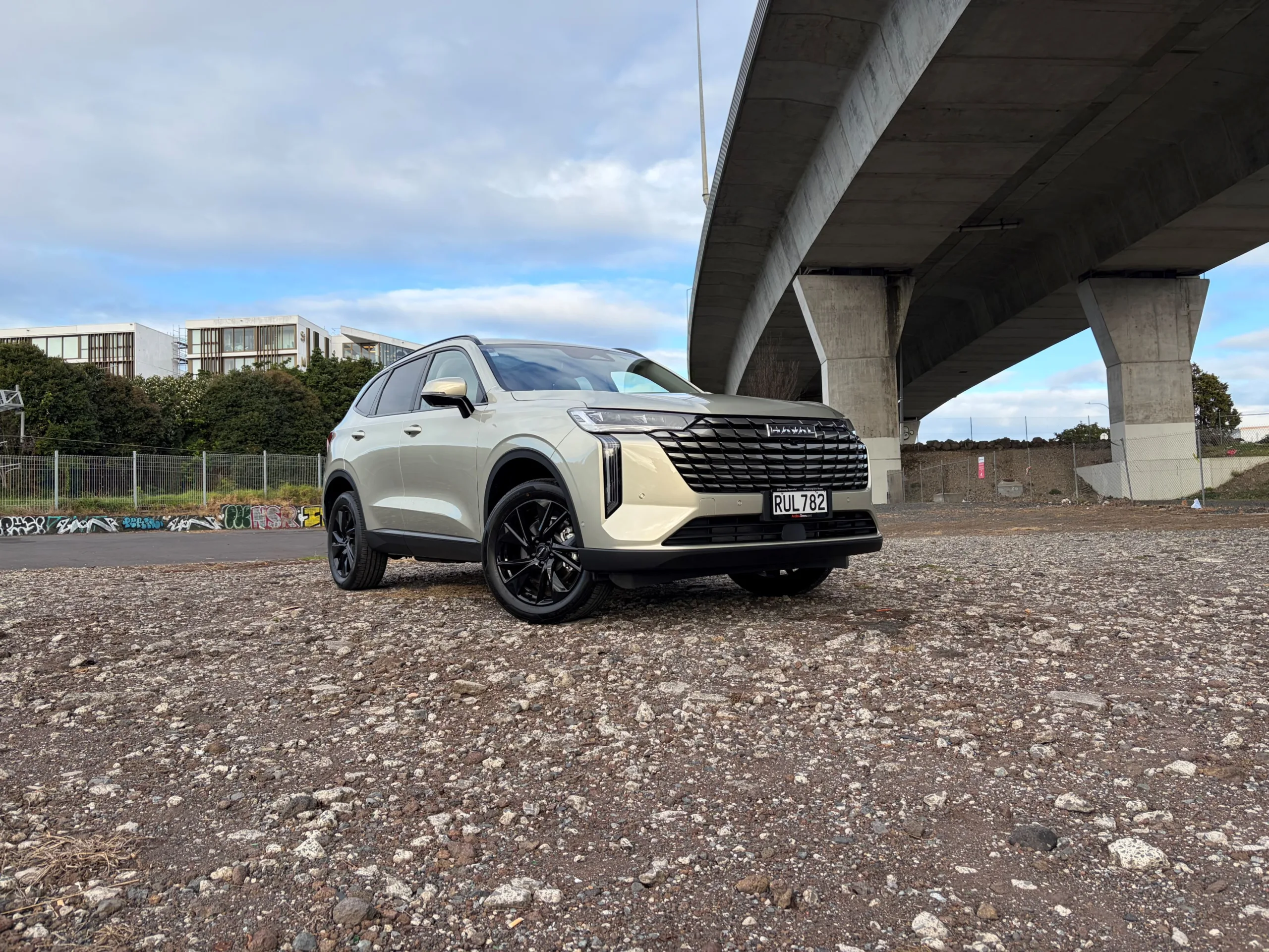 Front three quarters view of a 2026 GWM Haval H6 HEV in Astral Pearl, photographed against an urban backdrop.