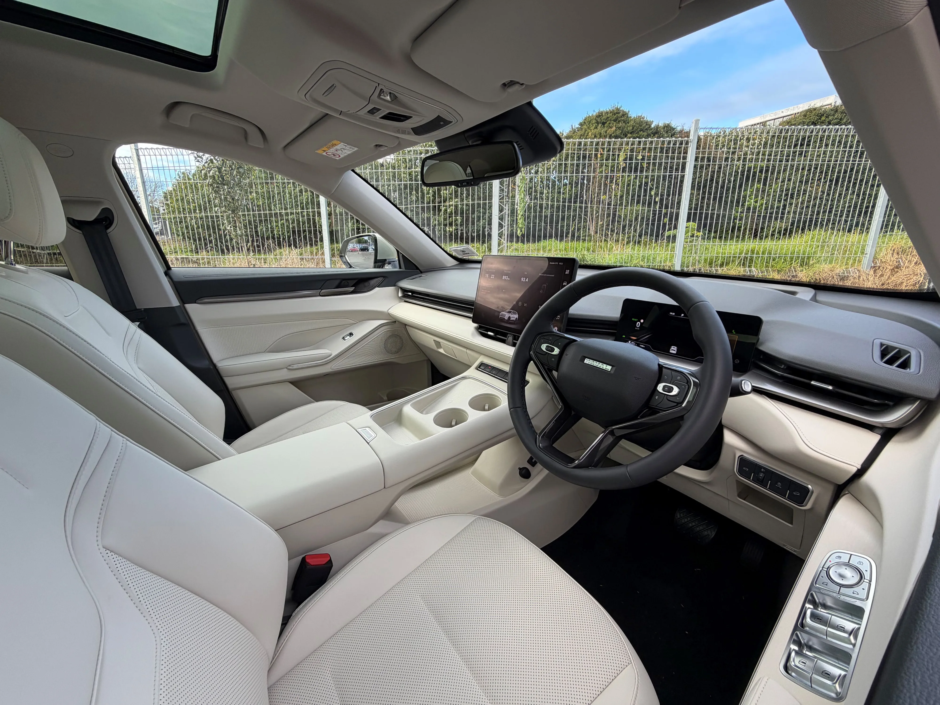 Interior view of a 2026 GWM Haval H6 HEV in Astral Pearl, photographed with an urban backdrop visible through the windscreen.