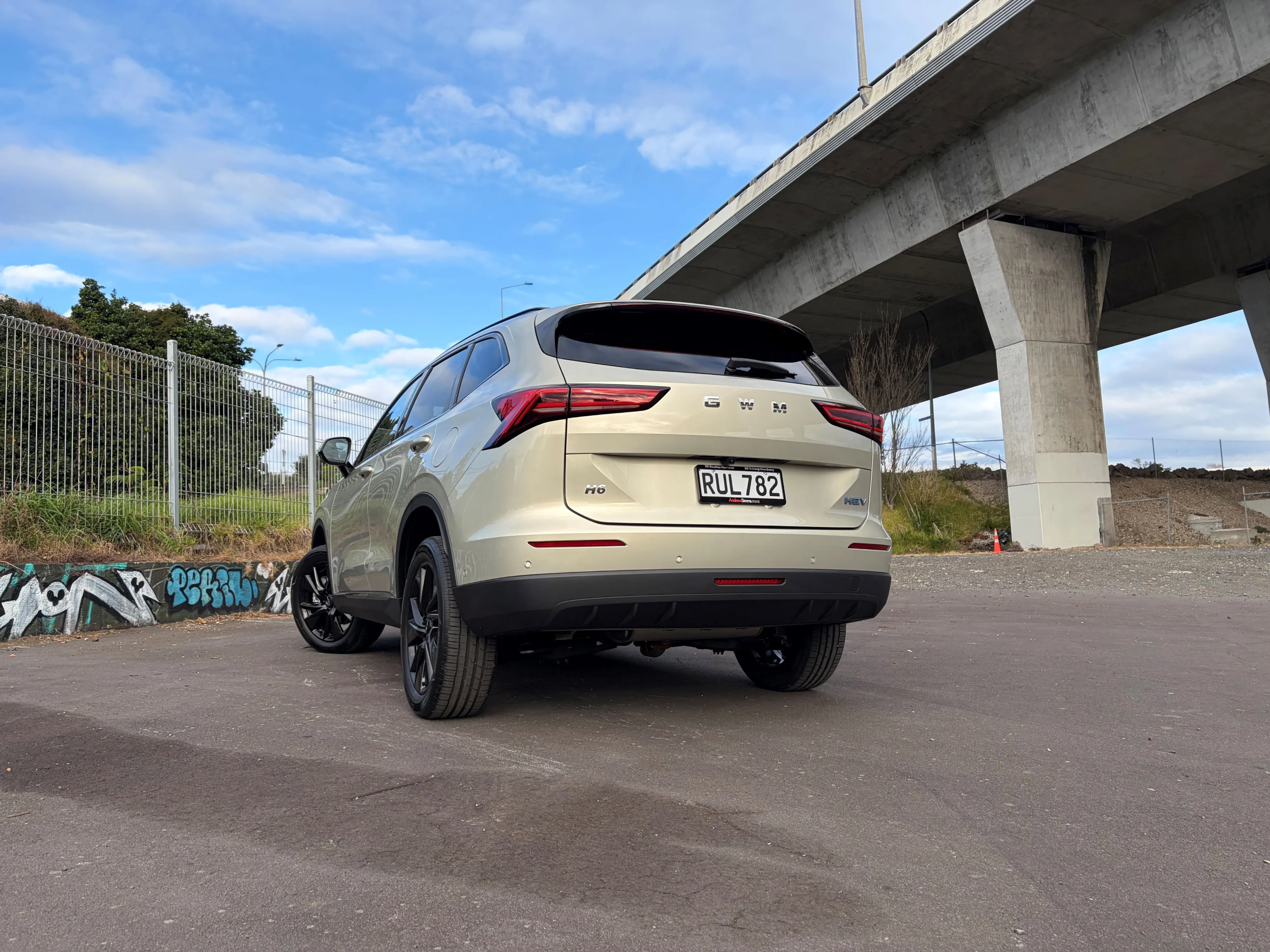 Rear three quarters view of a 2026 GWM Haval H6 HEV in Astral Pearl, photographed against an urban backdrop.